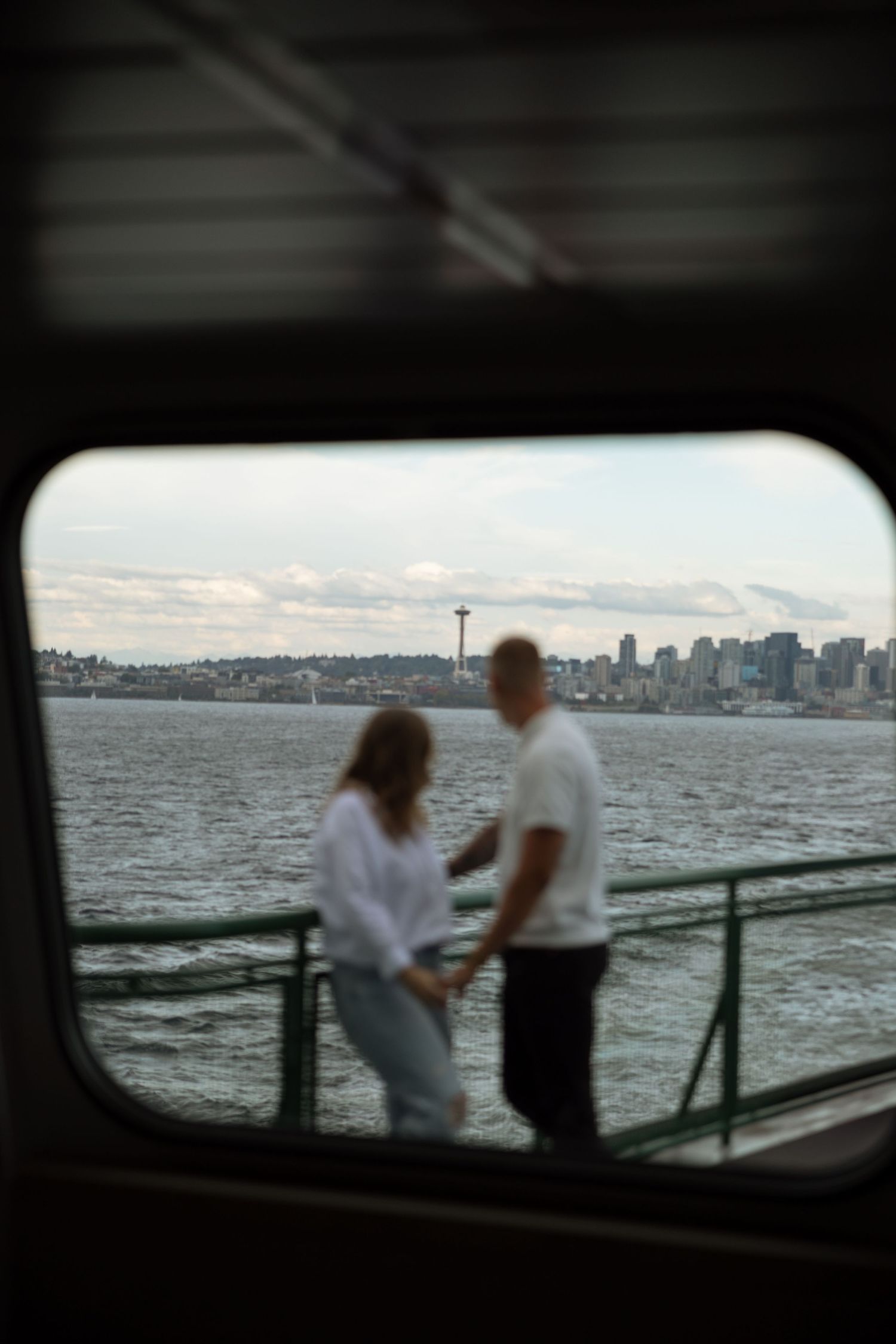 Silhouetted figures viewed through ferry window with Seattle skyline backdrop.
