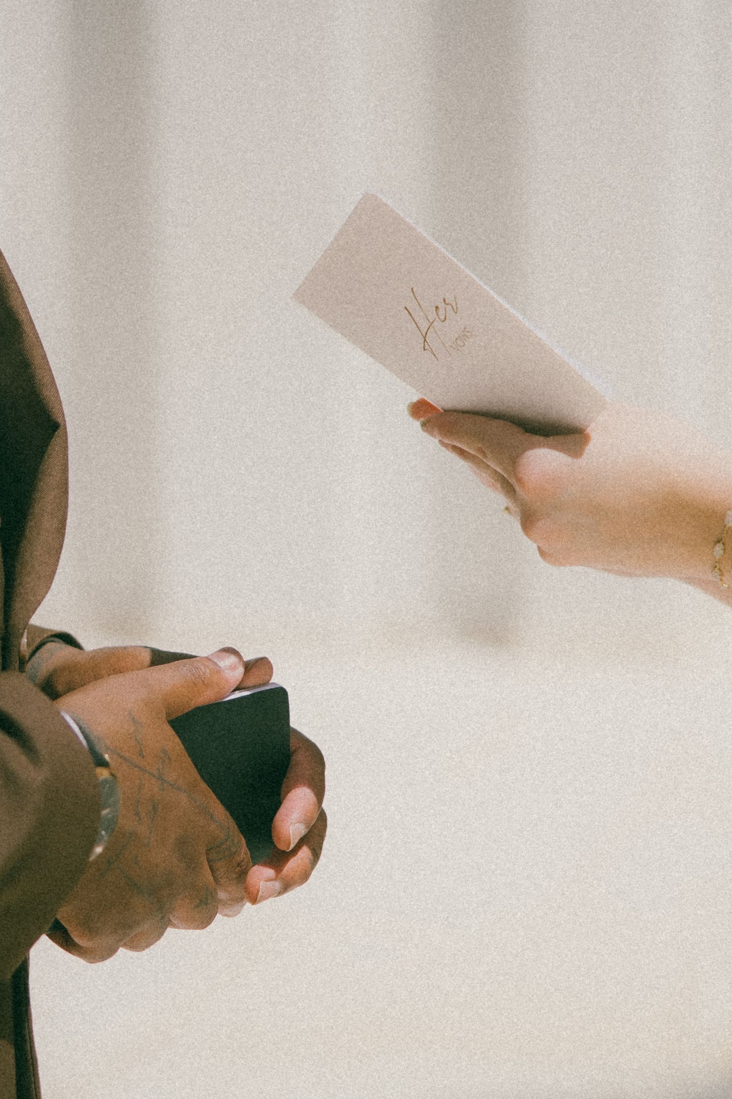 Close-up of hands exchanging wedding vows written on paper against a light background.