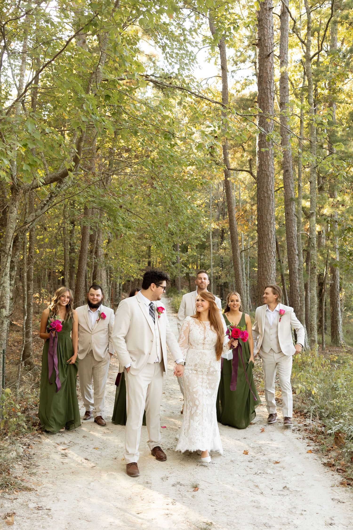 Joyful wedding party walking and laughing together on woodland trail with autumn foliage.