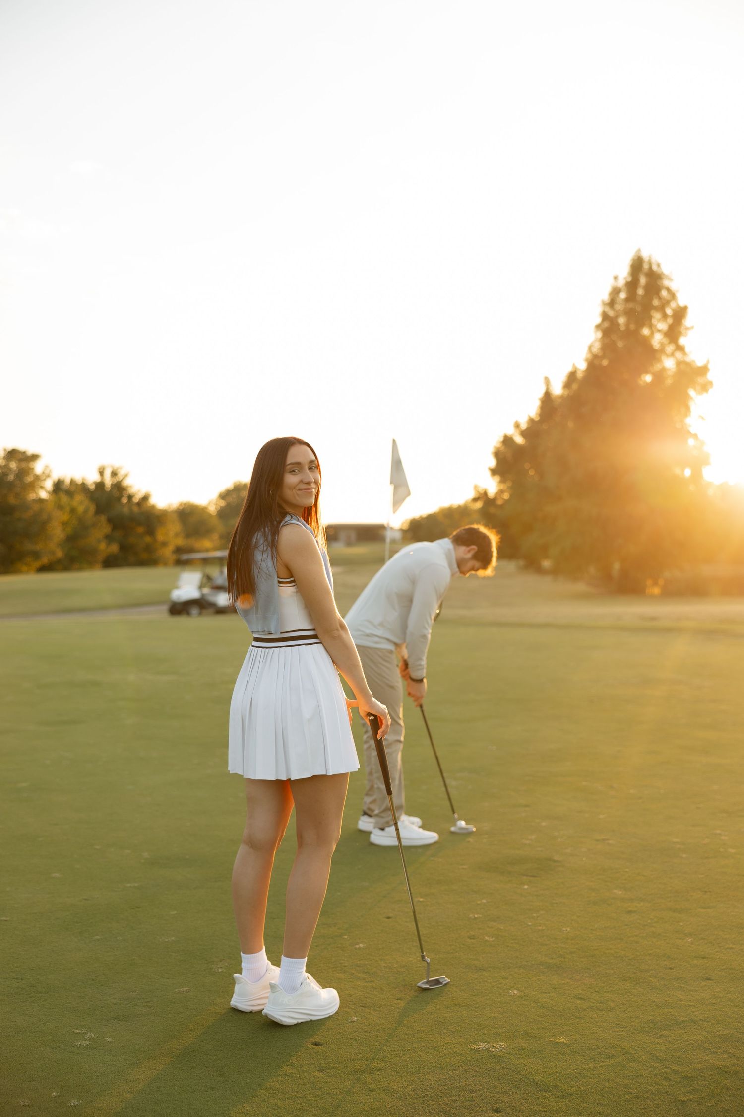 A couple playing golf together on a scenic course during golden hour sunset.