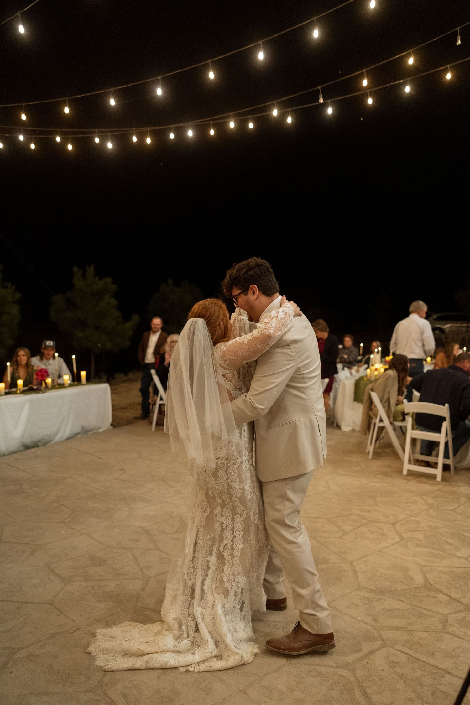 A romantic first dance moment beneath string lights at an outdoor wedding reception.