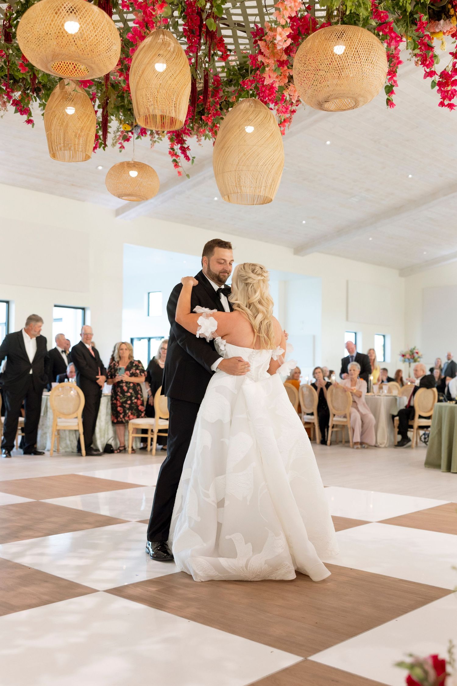 Wedding reception dance floor with hanging floral baskets and couples dancing in an elegant white room.