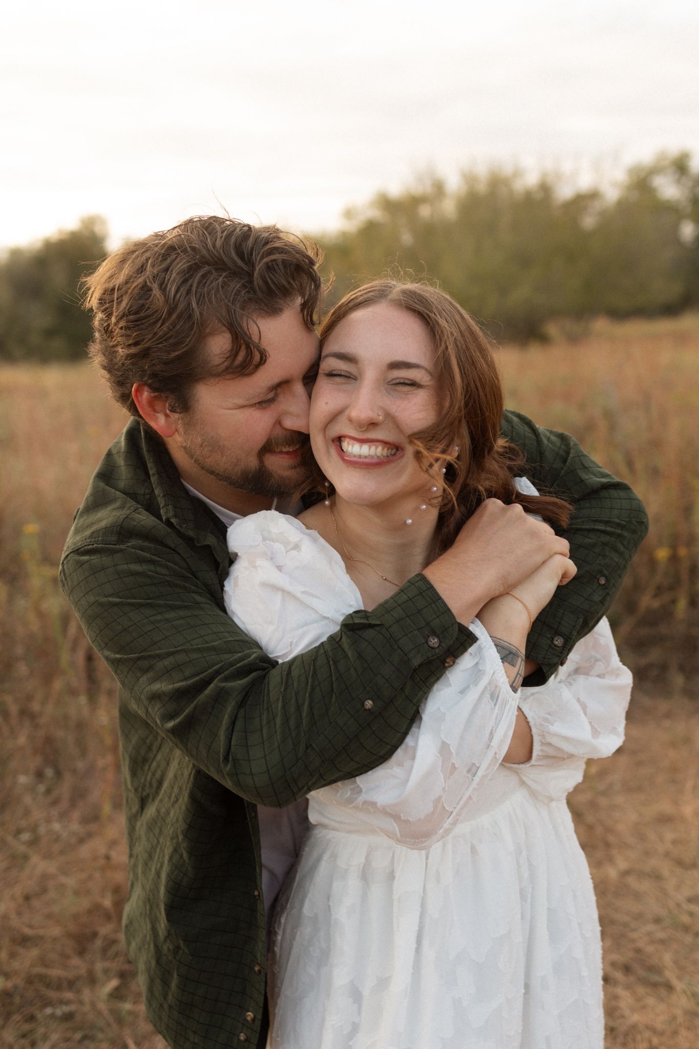 Romantic embrace captured during autumn sunset engagement session in rustic field.