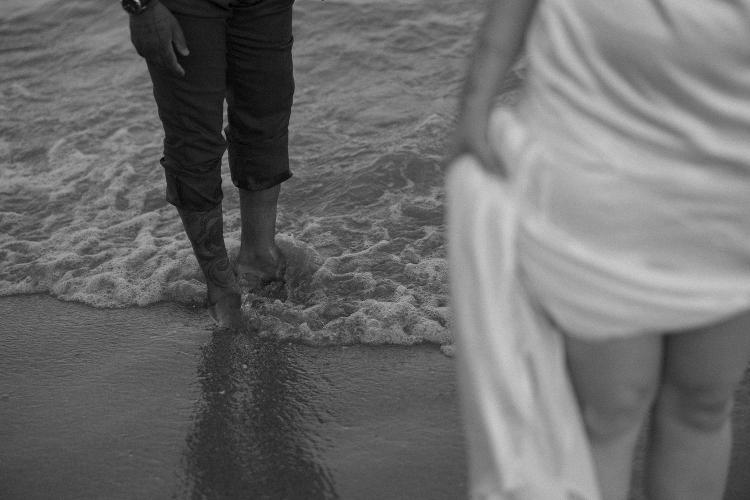 Close-up shot of feet in shallow ocean waves on a sandy beach.