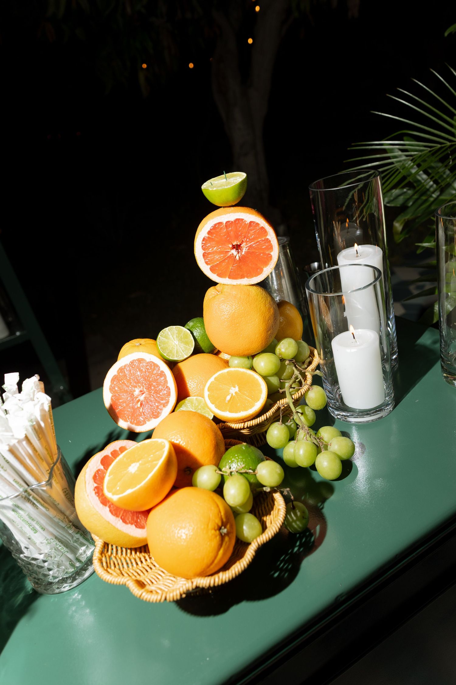 Decorative wedding bar display with fresh citrus fruits, grapes, and white candles at night.