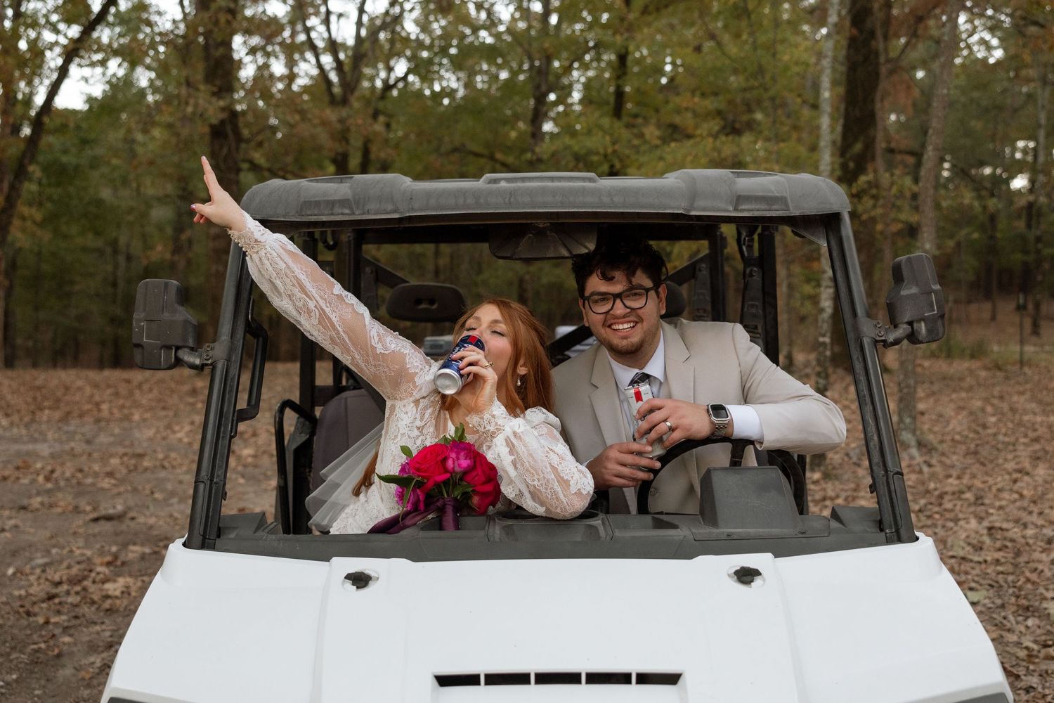 Newlyweds celebrate in a golf cart while holding wedding bouquet and beverages.