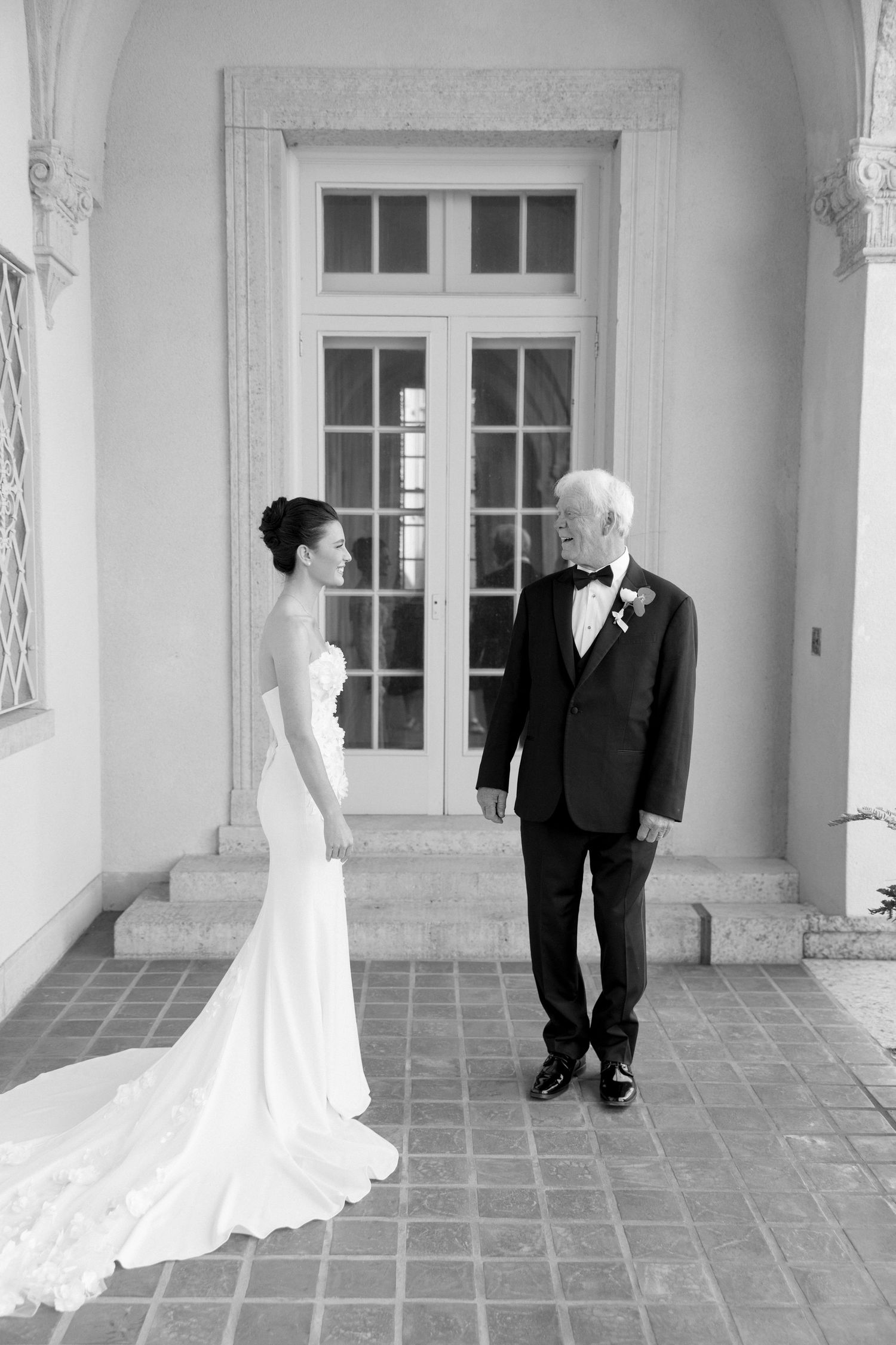 Black and white photo of a bride in a sleek gown sharing a first look moment with her father outside a venue.