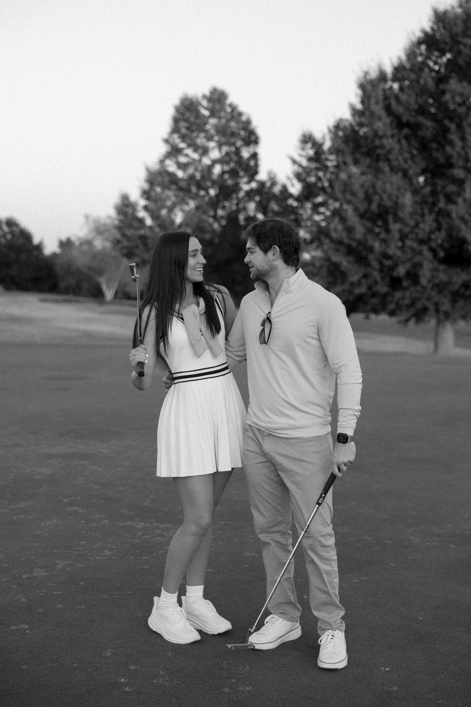 A couple in matching white outfits sharing a moment on a golf course.