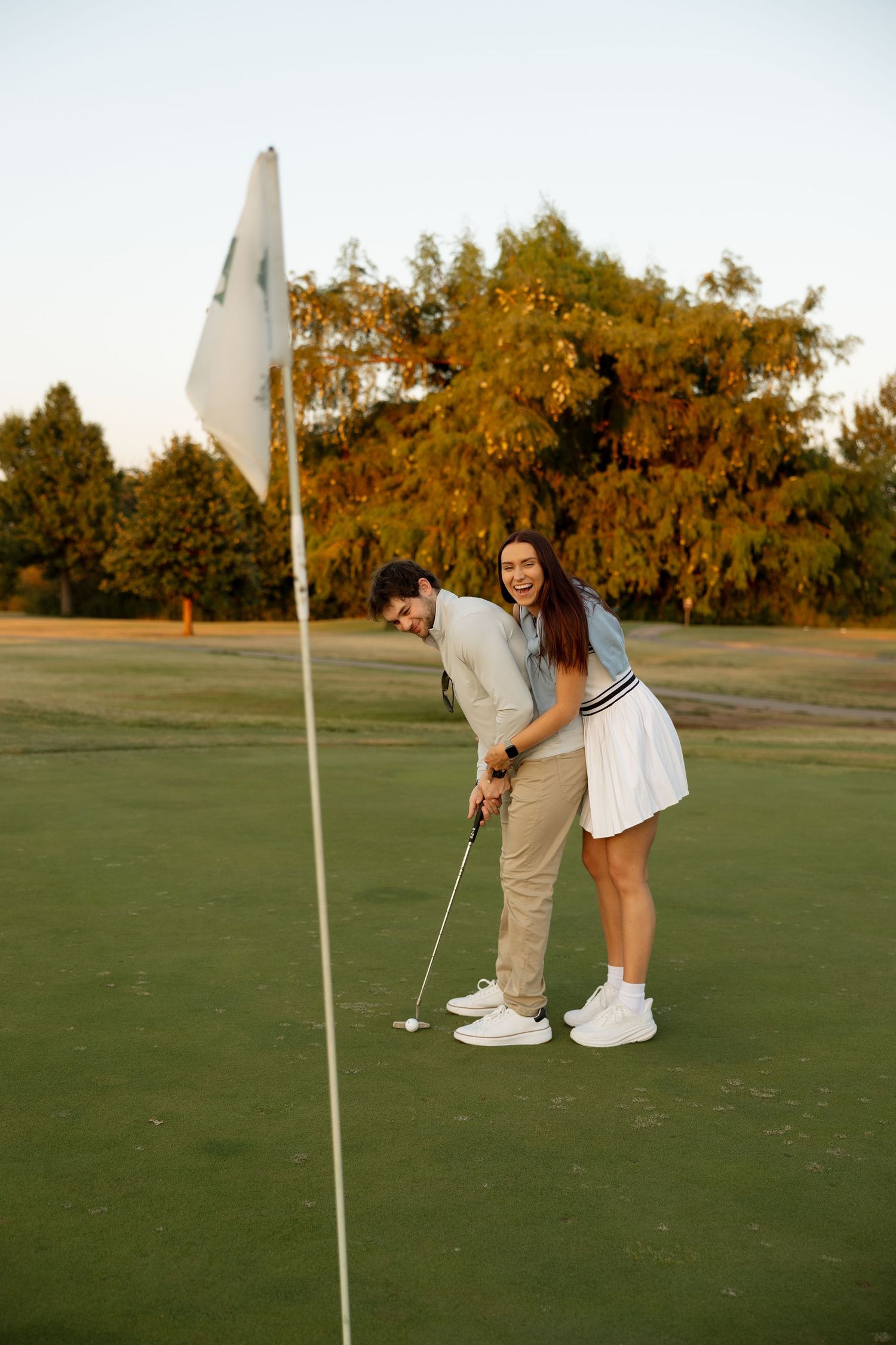 Playful golf lesson scene with couple laughing by the flag pole.
