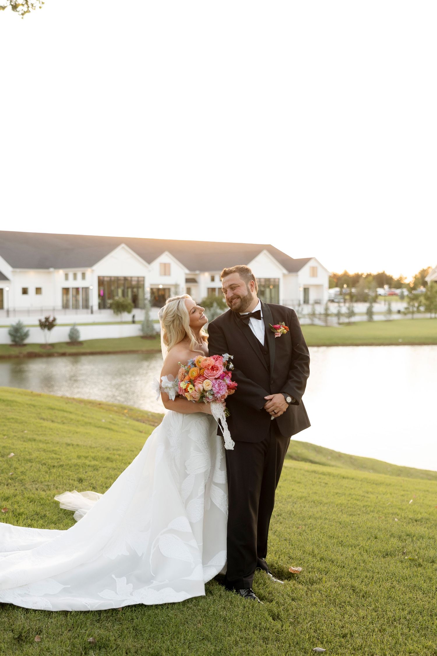 Outdoor wedding portraits at sunset with white houses and lake in background.