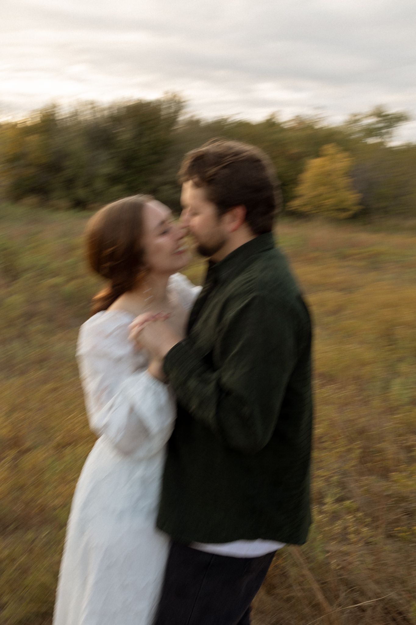 A blurred motion shot captures a tender moment between a couple in an autumn field.
