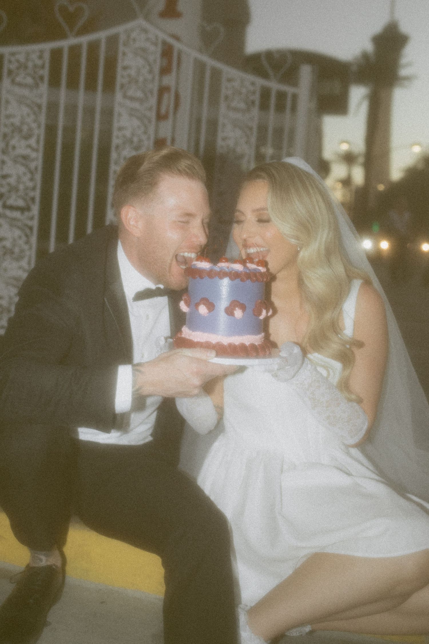 Newlyweds share a playful moment eating a small purple wedding cake outside the Little White Chapel in Las Vegas.