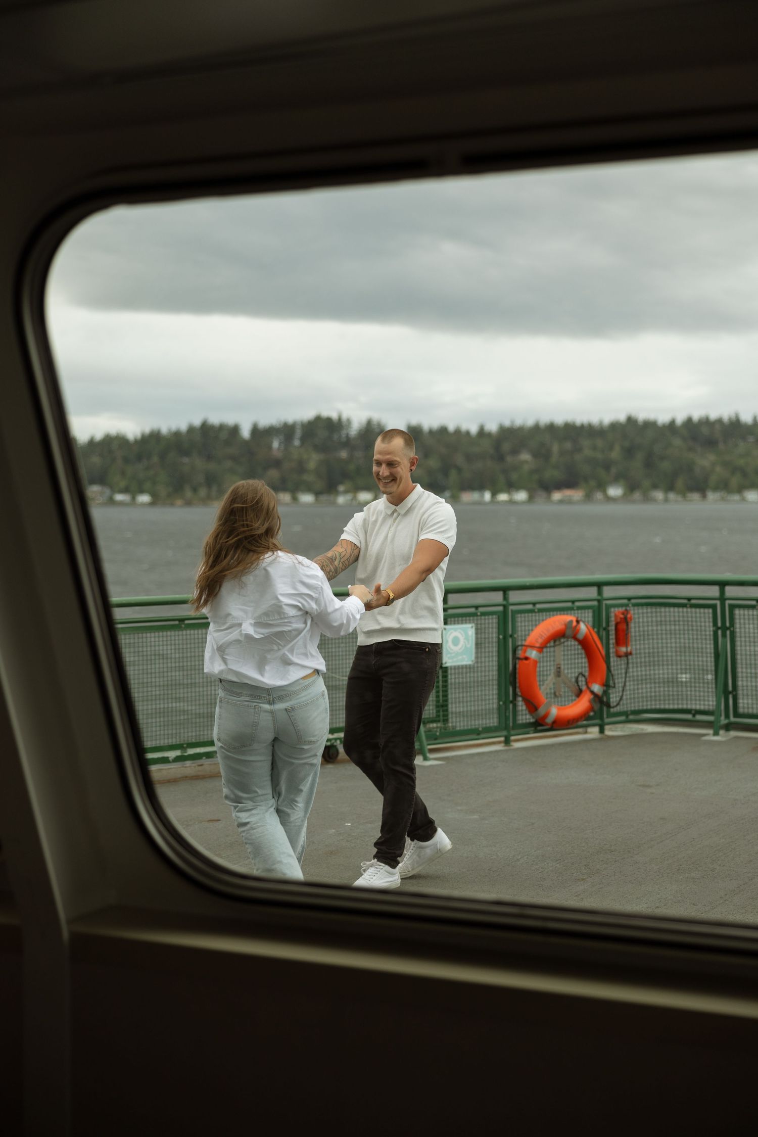 Passengers on ferry deck with life preserver and waterfront view.
