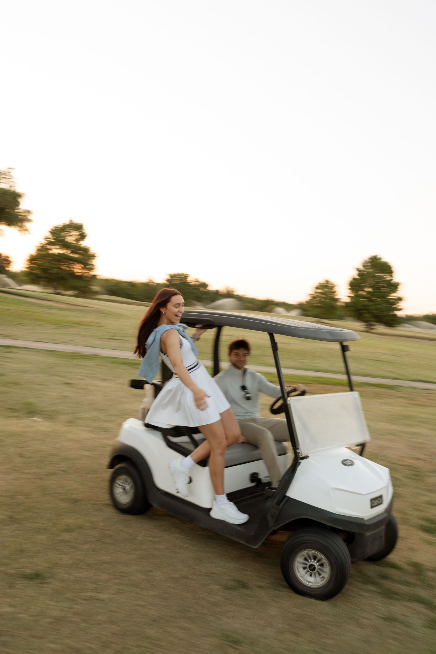 A couple having fun riding in a golf cart across the course at golden hour.
