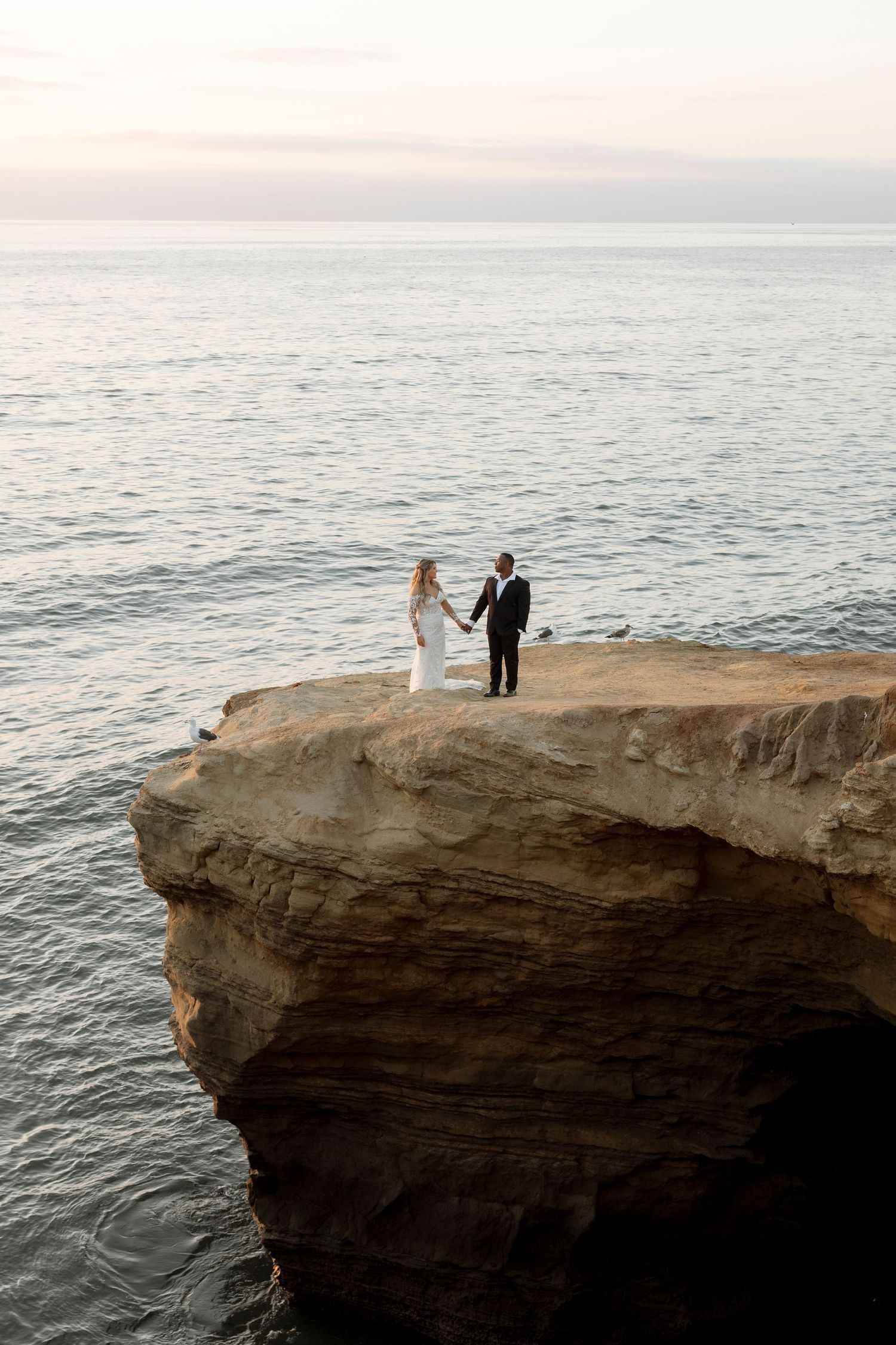 A couple stands on a dramatic ocean cliff during sunset for wedding photos.
