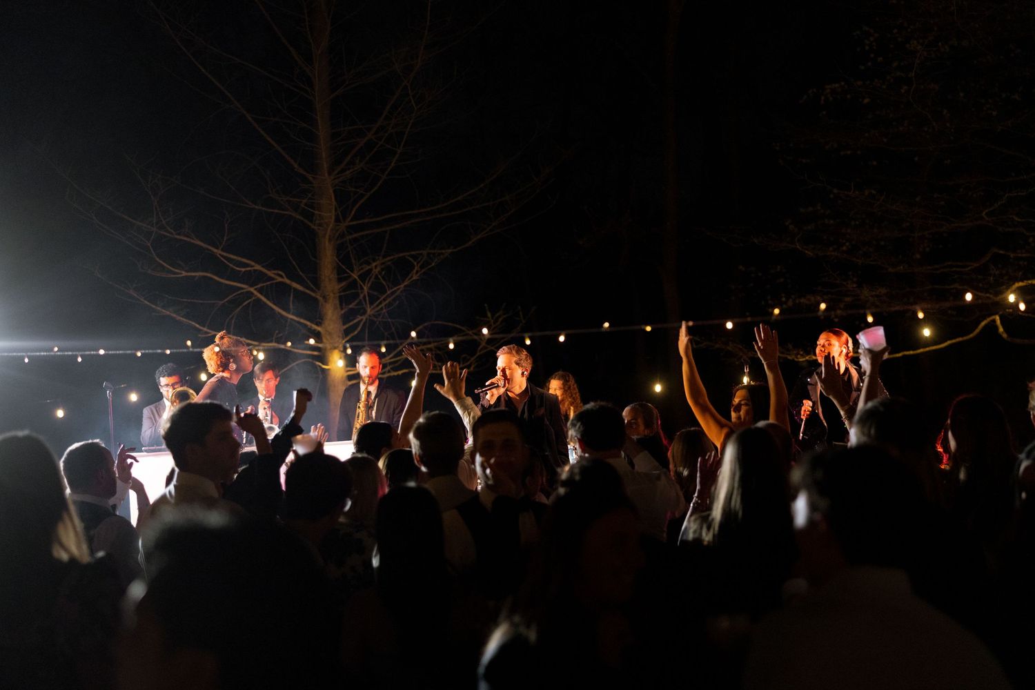 Guests celebrating at an outdoor wedding reception under string lights at night.
