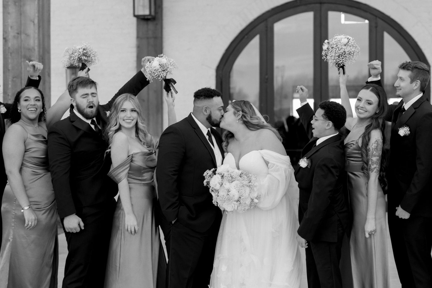 A wedding party celebrates with the newlyweds in a black and white photo.