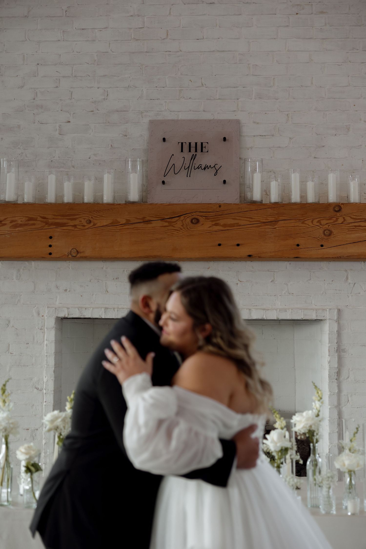 Intimate moment between newlyweds beneath rustic wooden mantle decorated with candlelight.