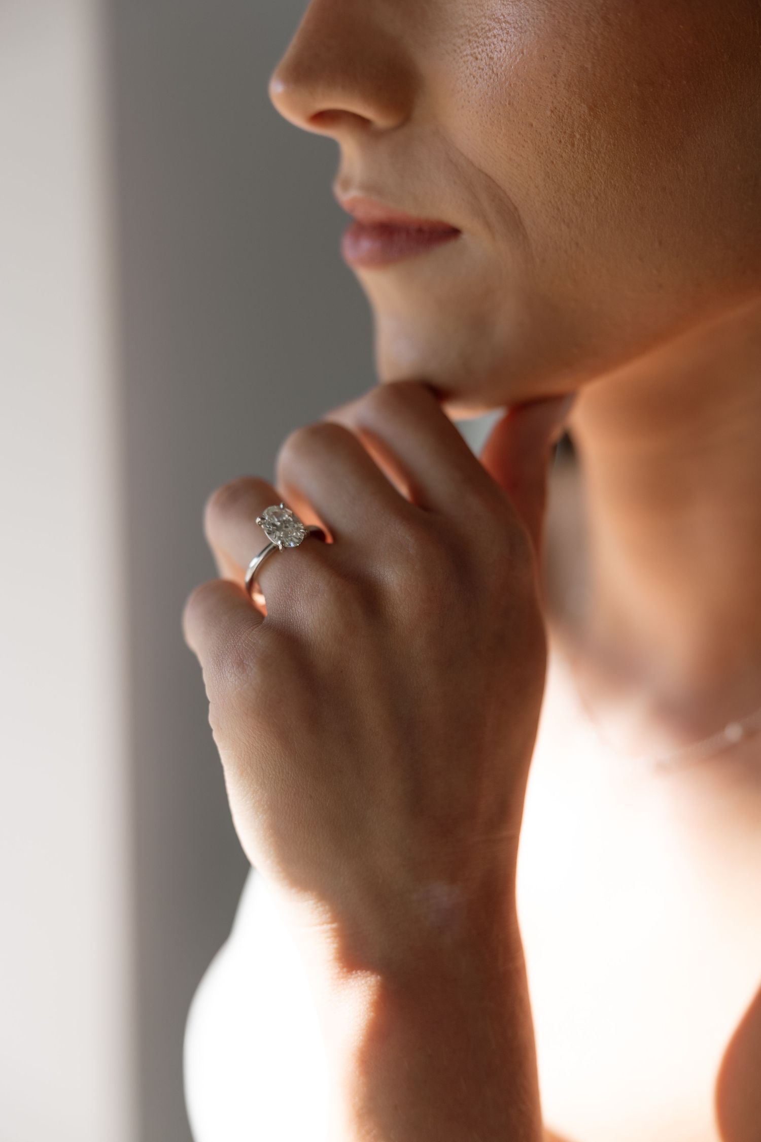 Close-up profile shot showing a hand with an engagement ring touching chin in soft natural lighting.