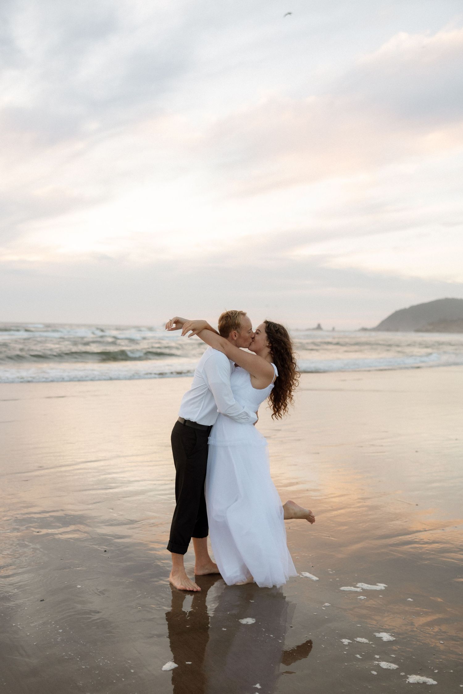 A joyful embrace on the beach at sunset with waves crashing in the background.