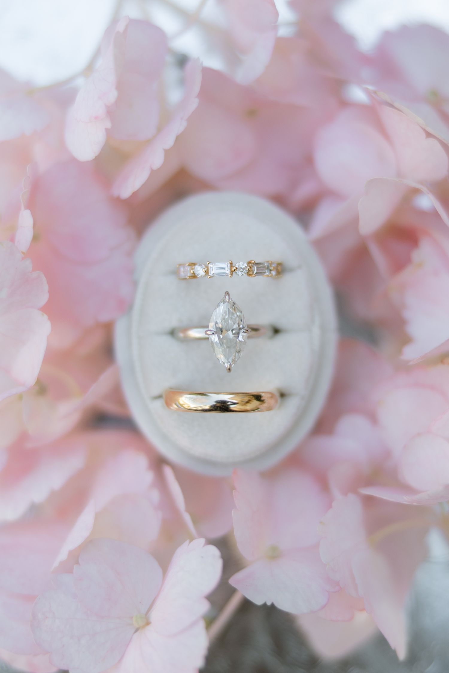 Three gold wedding rings, including a marquise diamond engagement ring, rest in a velvet ring box.