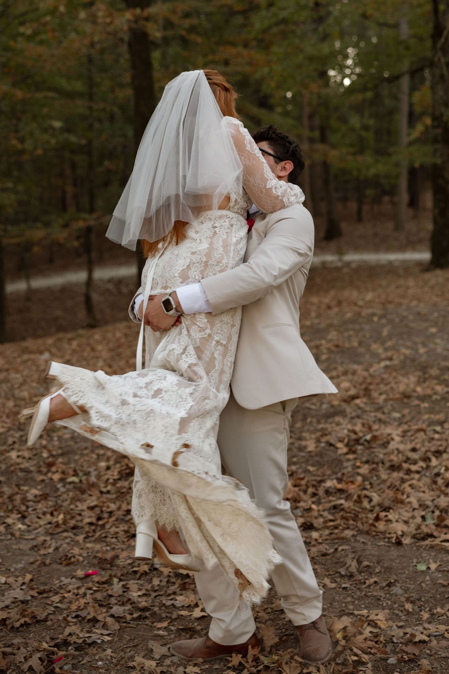 A playful wedding moment captured as the couple twirls among fallen leaves in the forest.
