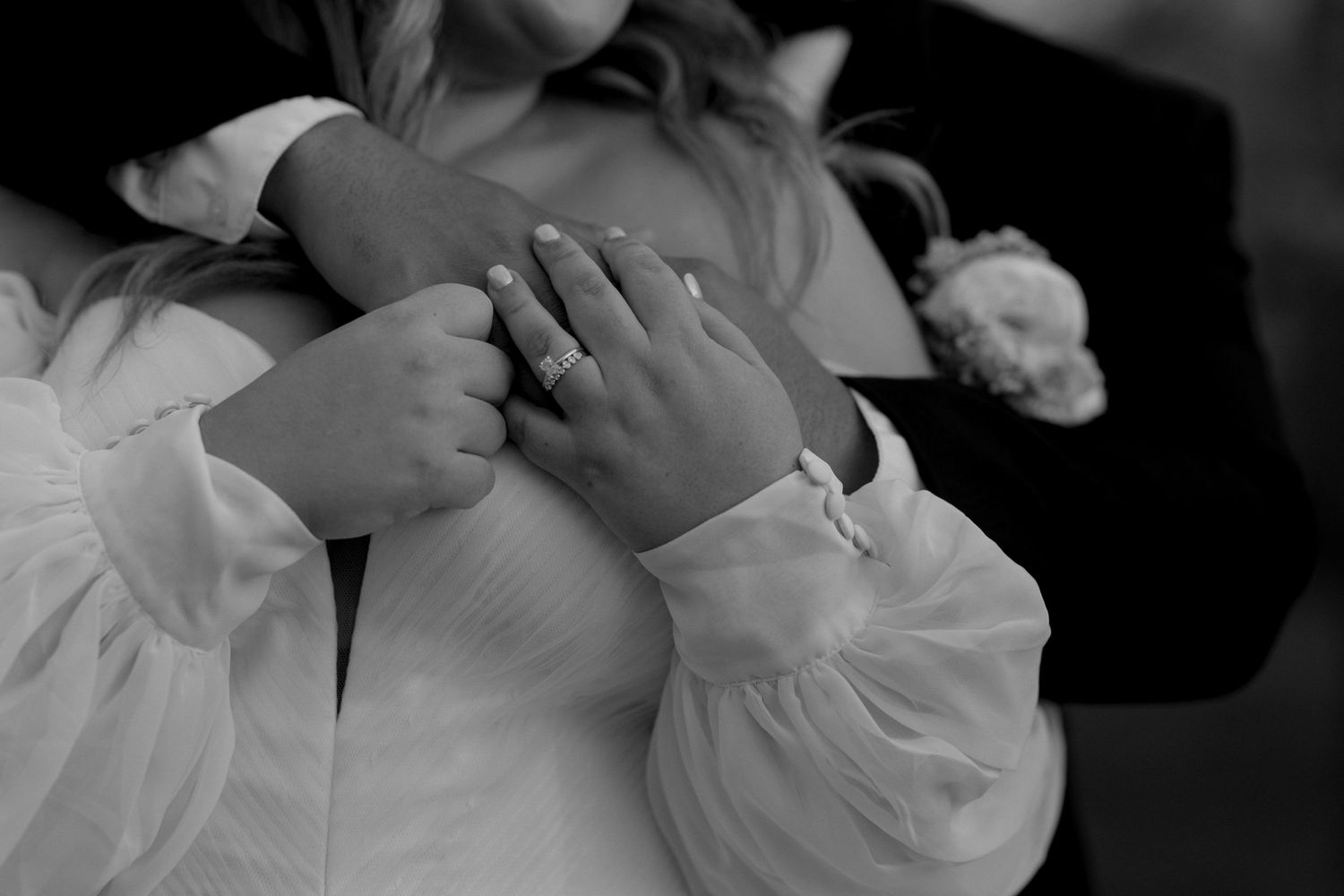 A black and white detail shot of hands and wedding attire.