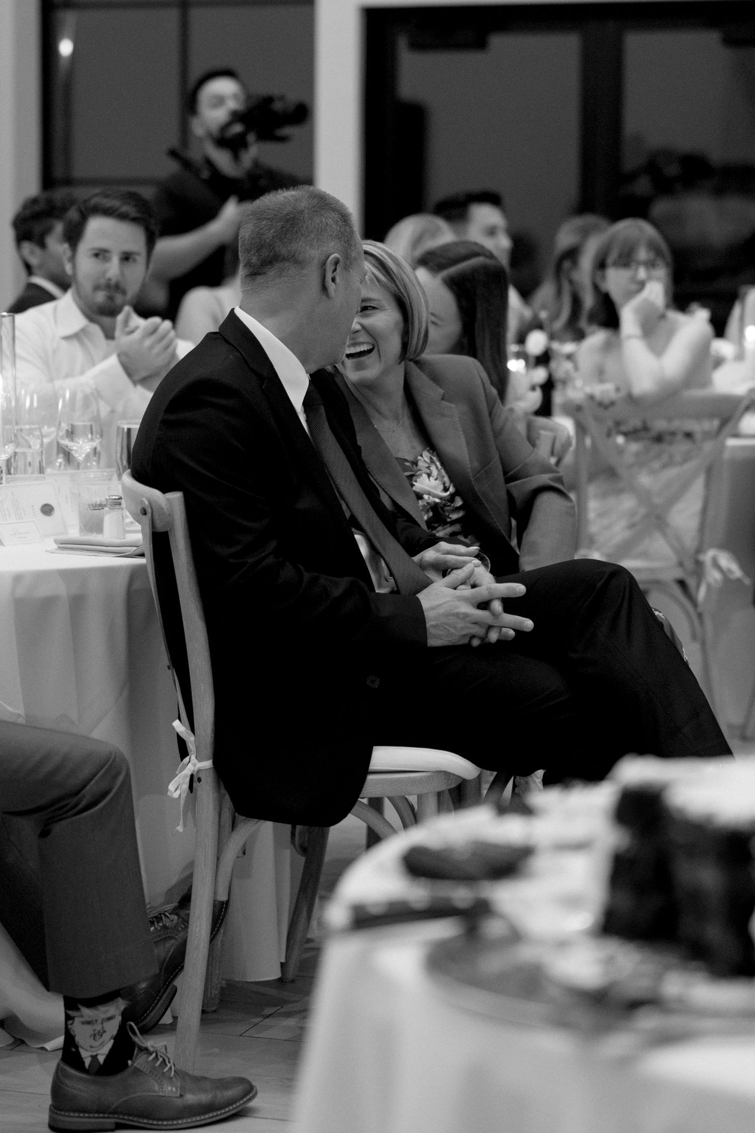 Black and white photo of wedding guests laughing and enjoying the reception celebration.