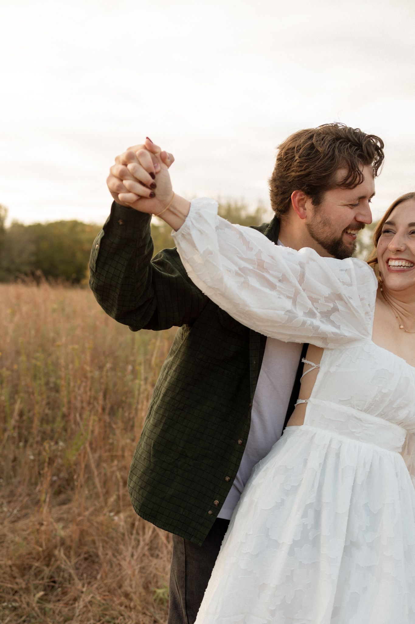 Couple dances together in autumn field during golden hour photo session.