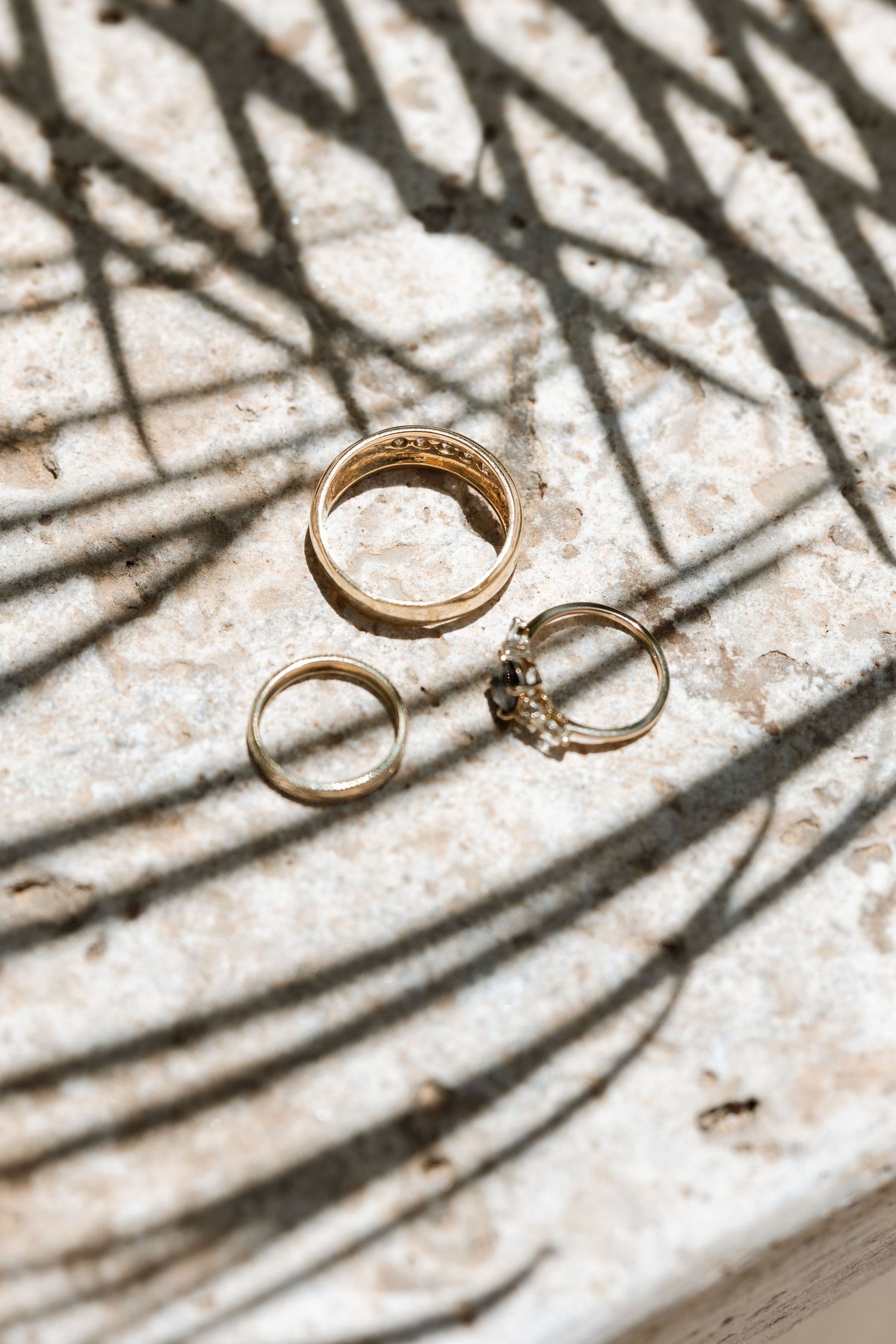 Gold wedding rings casting intricate shadows on a textured white surface.