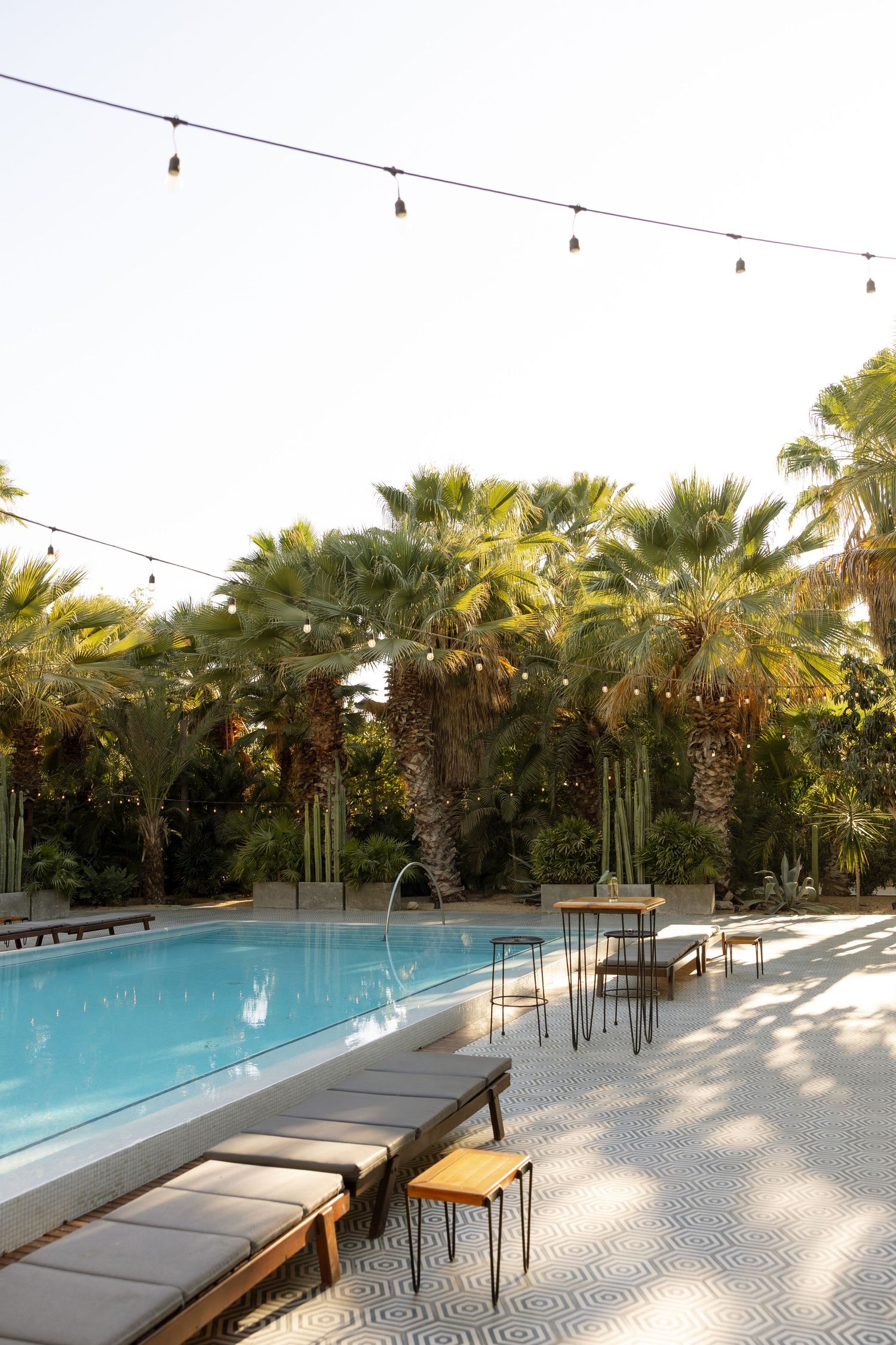 Elegant outdoor pool venue with string lights, lounge chairs, and lush palm trees at dusk.