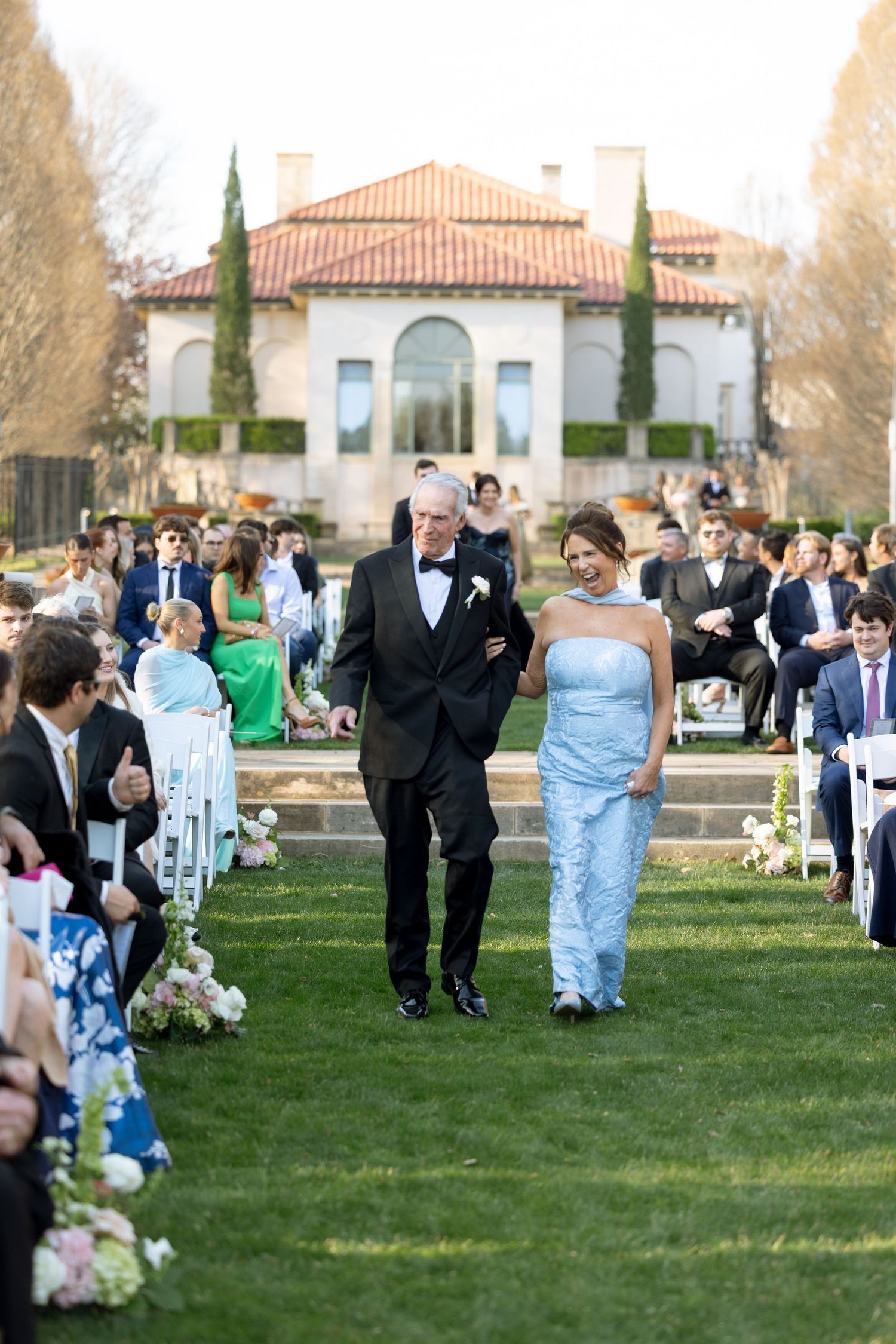 Bride in light blue gown walks down the aisle with her father at an outdoor wedding.