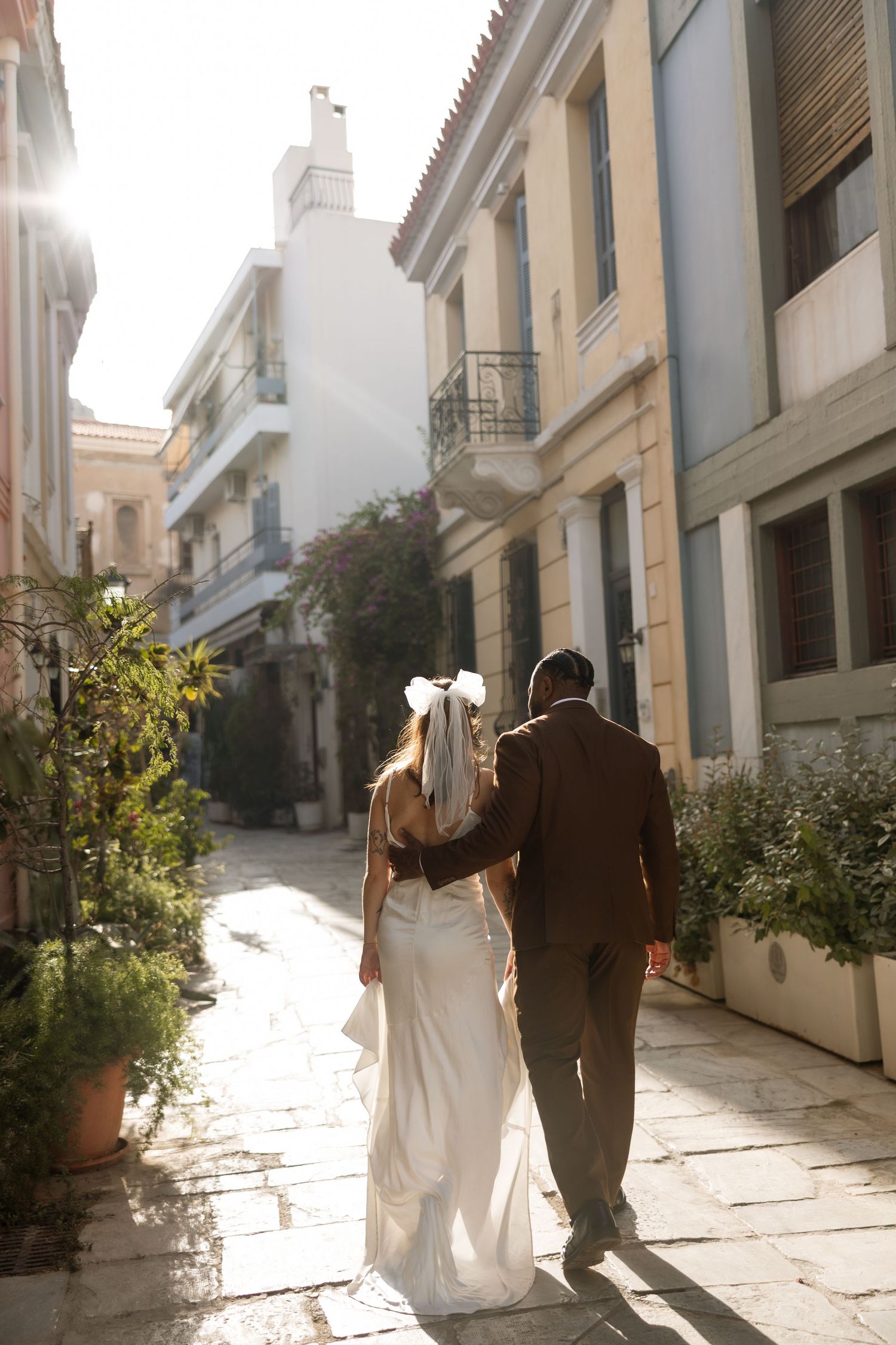 Sun-drenched photo of couple walking together down narrow European street with traditional architecture.