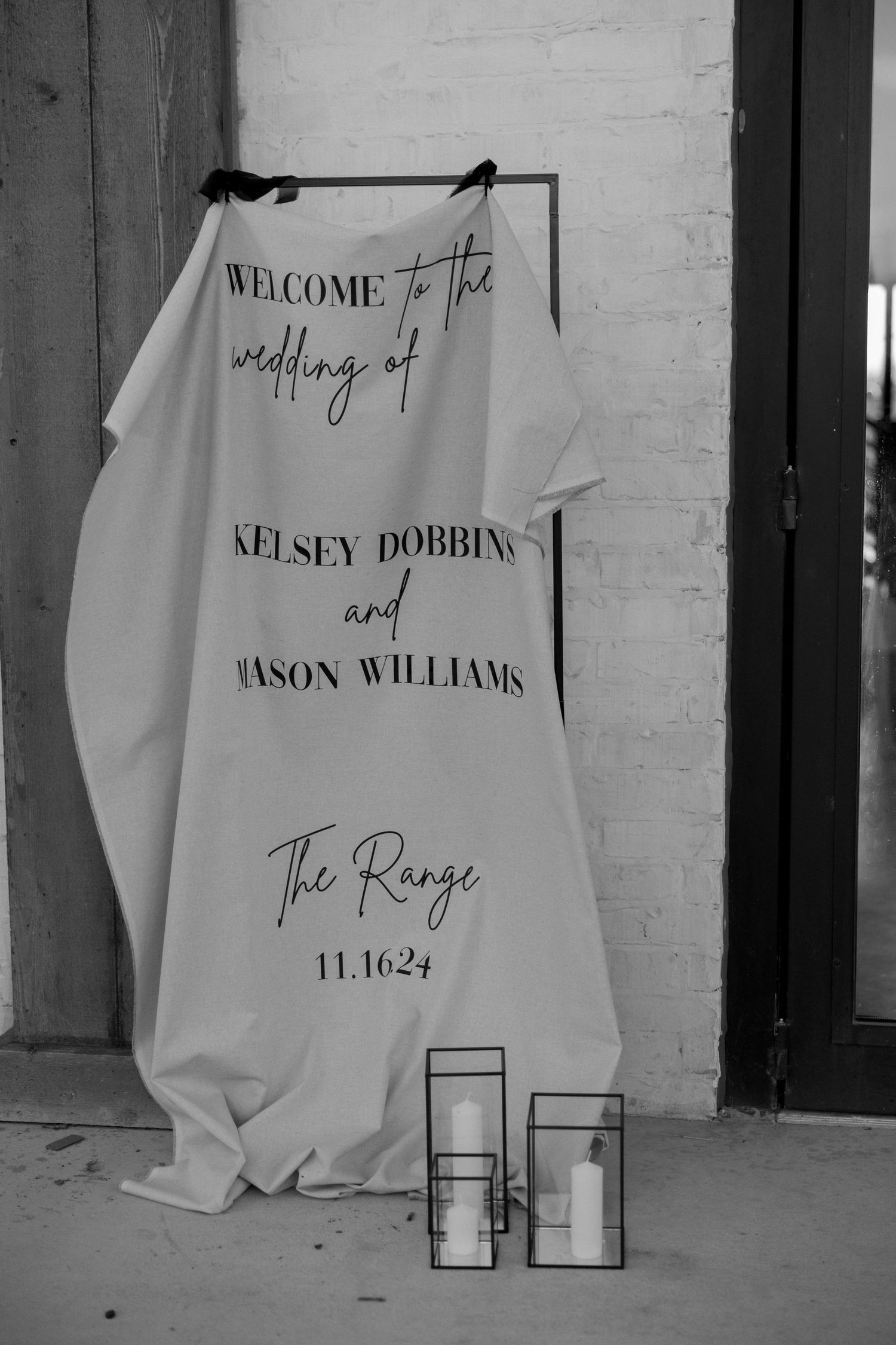 Wedding welcome sign on white fabric displaying event details with lanterns.