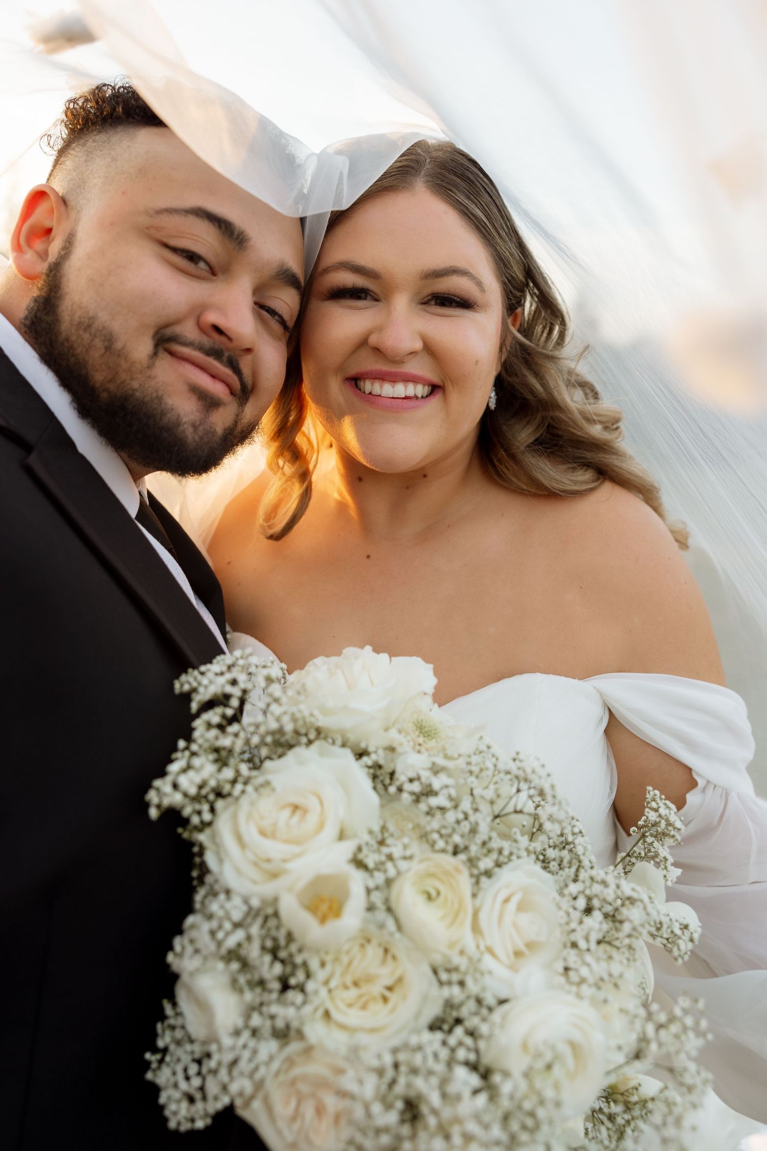 An intimate wedding portrait under a veil with white roses and baby's breath bouquet.