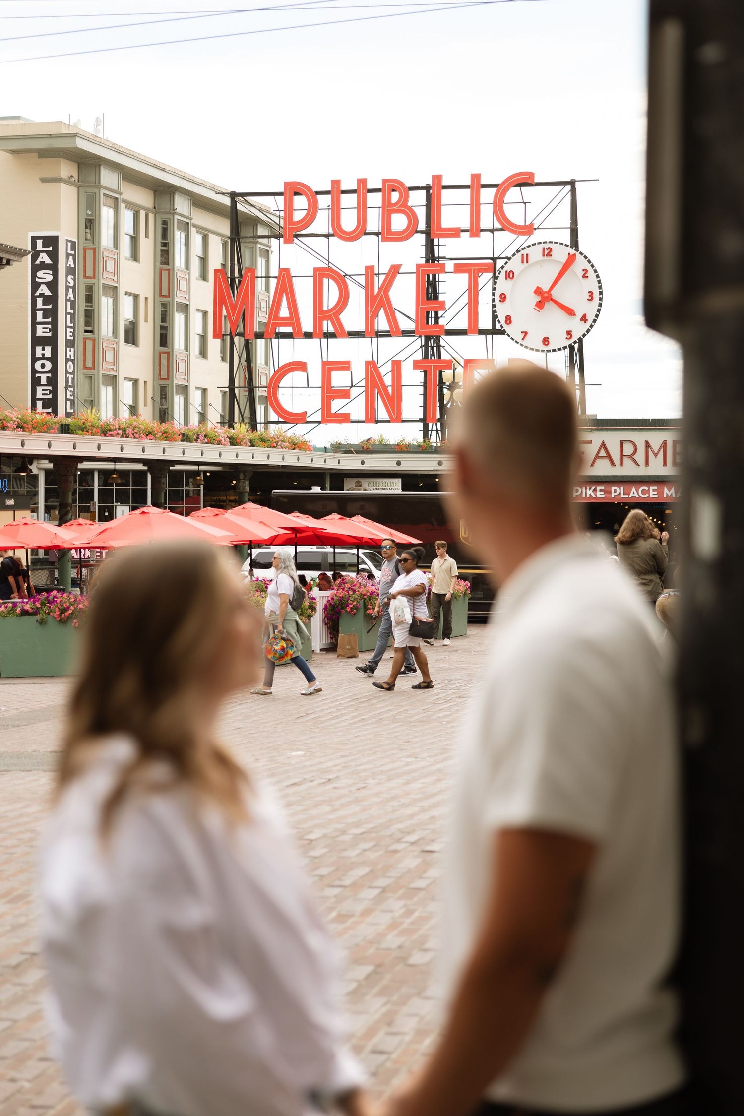 Visitors observe the bustling scene beneath Pike Place Market's famous red sign.