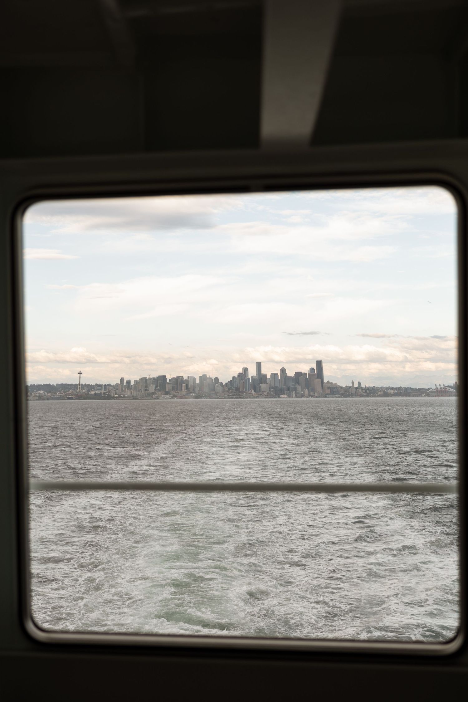 View of Seattle skyline across Elliott Bay seen through ferry window on overcast day.