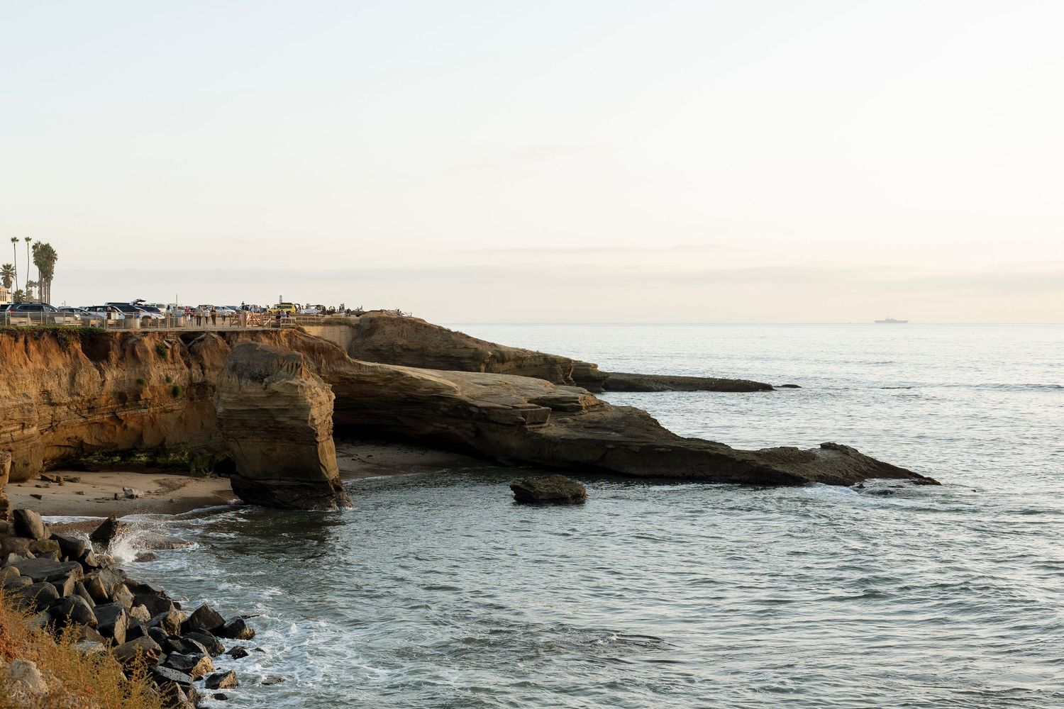Rugged coastal landscape with rocky cliffs and crashing waves along the Pacific Ocean at sunset.