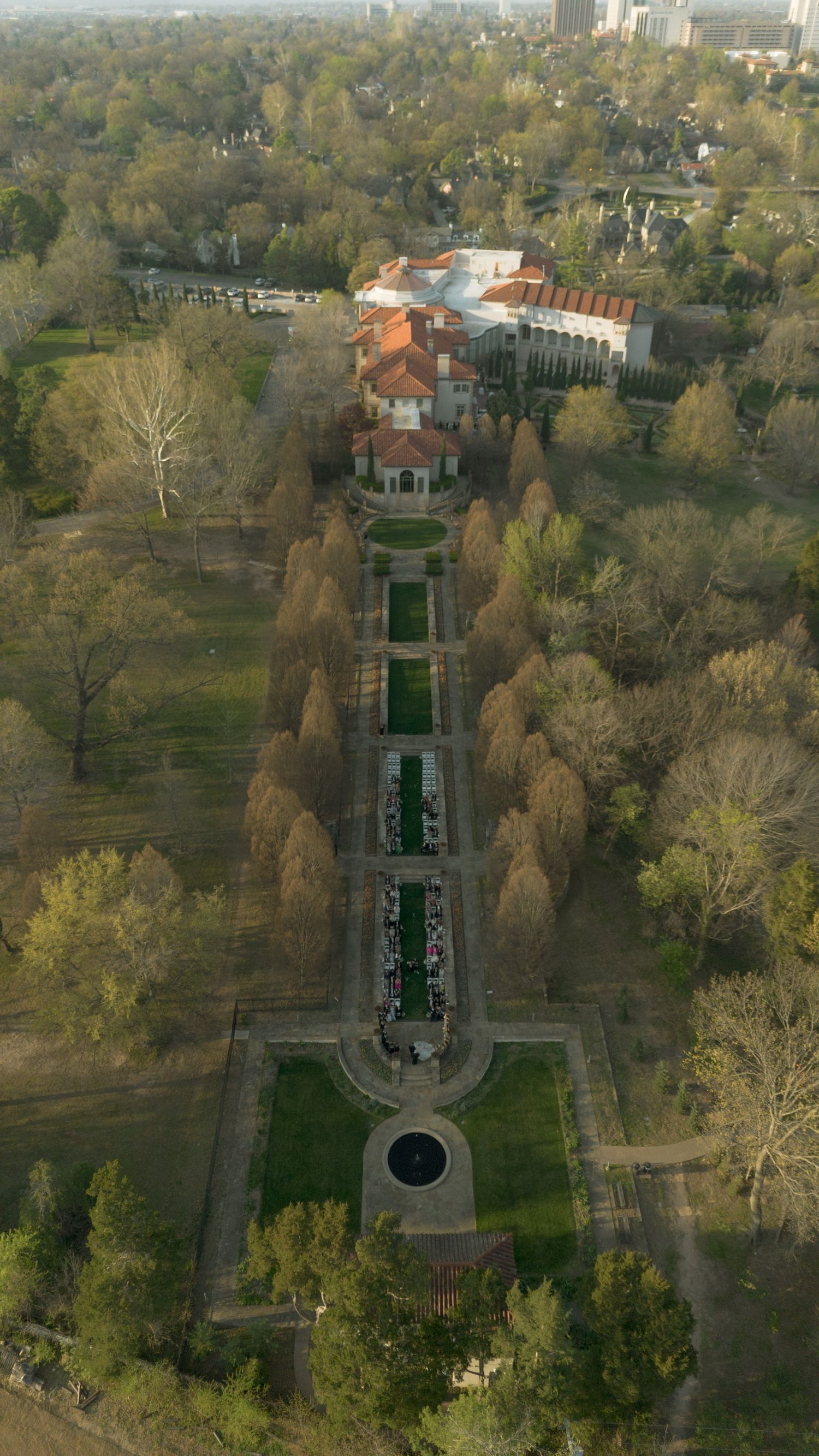 Aerial view of a grand estate with formal gardens and tree-lined pathways surrounded by lush greenery.