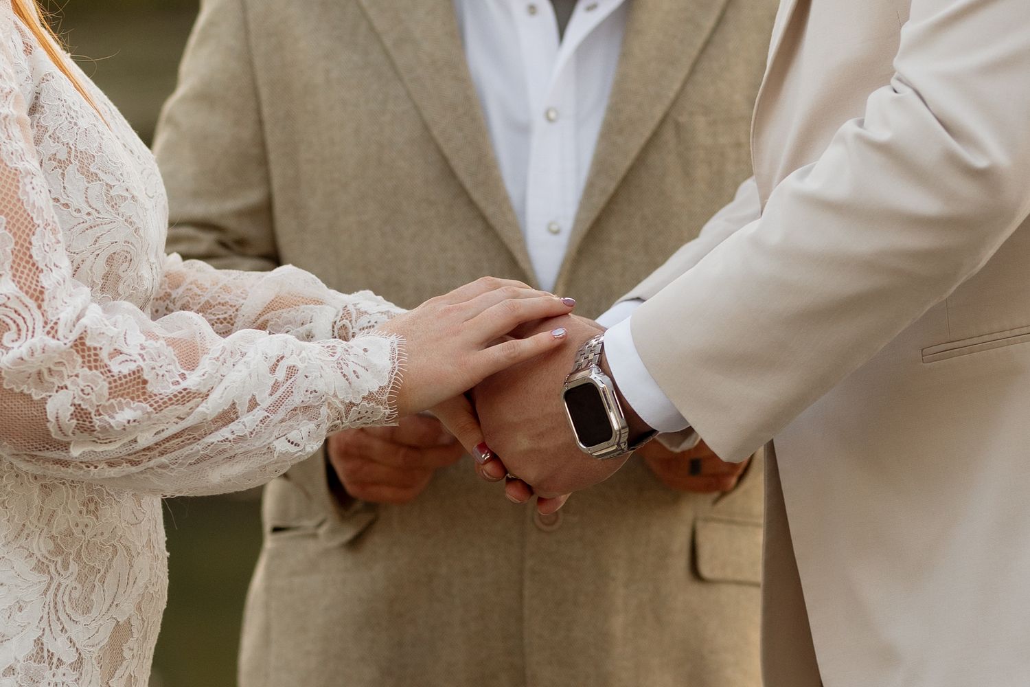 Close-up of hands with wedding rings and watch during ceremony.