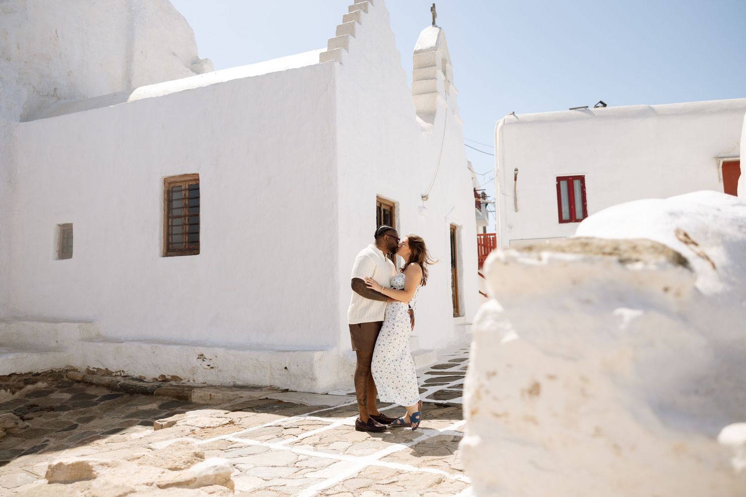 Woman in white dress walking through narrow white-walled Mediterranean alleyway.