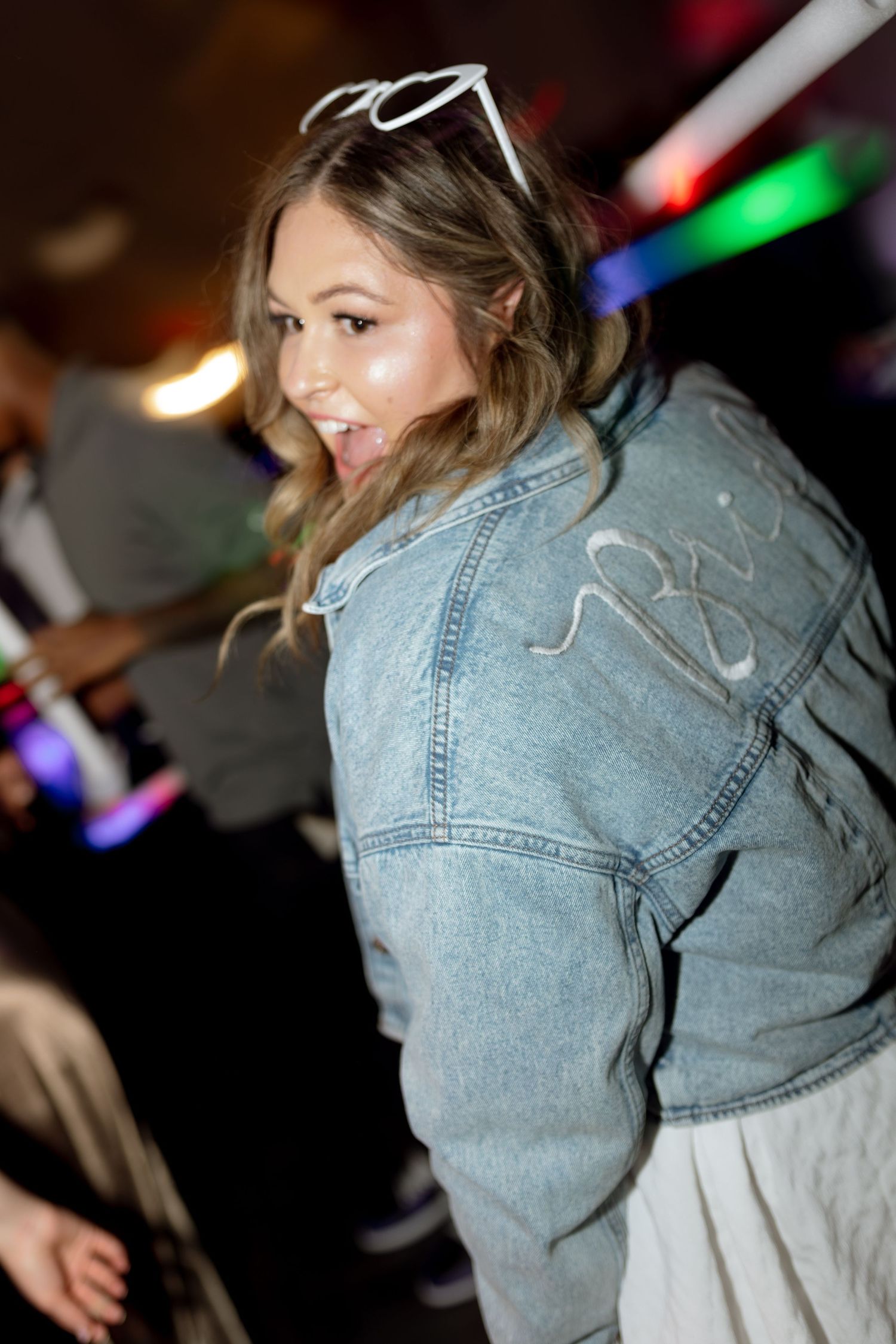 Person wearing a denim jacket and heart sunglasses dances joyfully at a wedding reception.