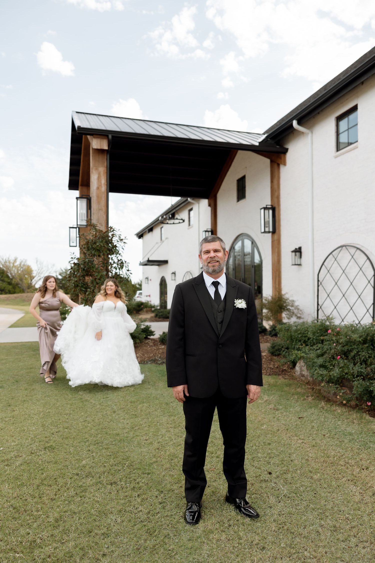 A formal wedding scene outside a modern white building with arched details.