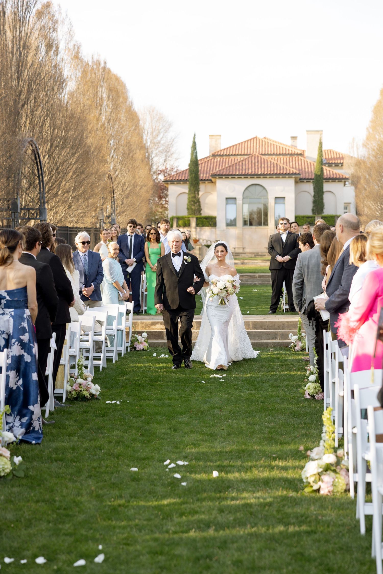 Bride walks down outdoor aisle with father at elegant Italian villa wedding venue.