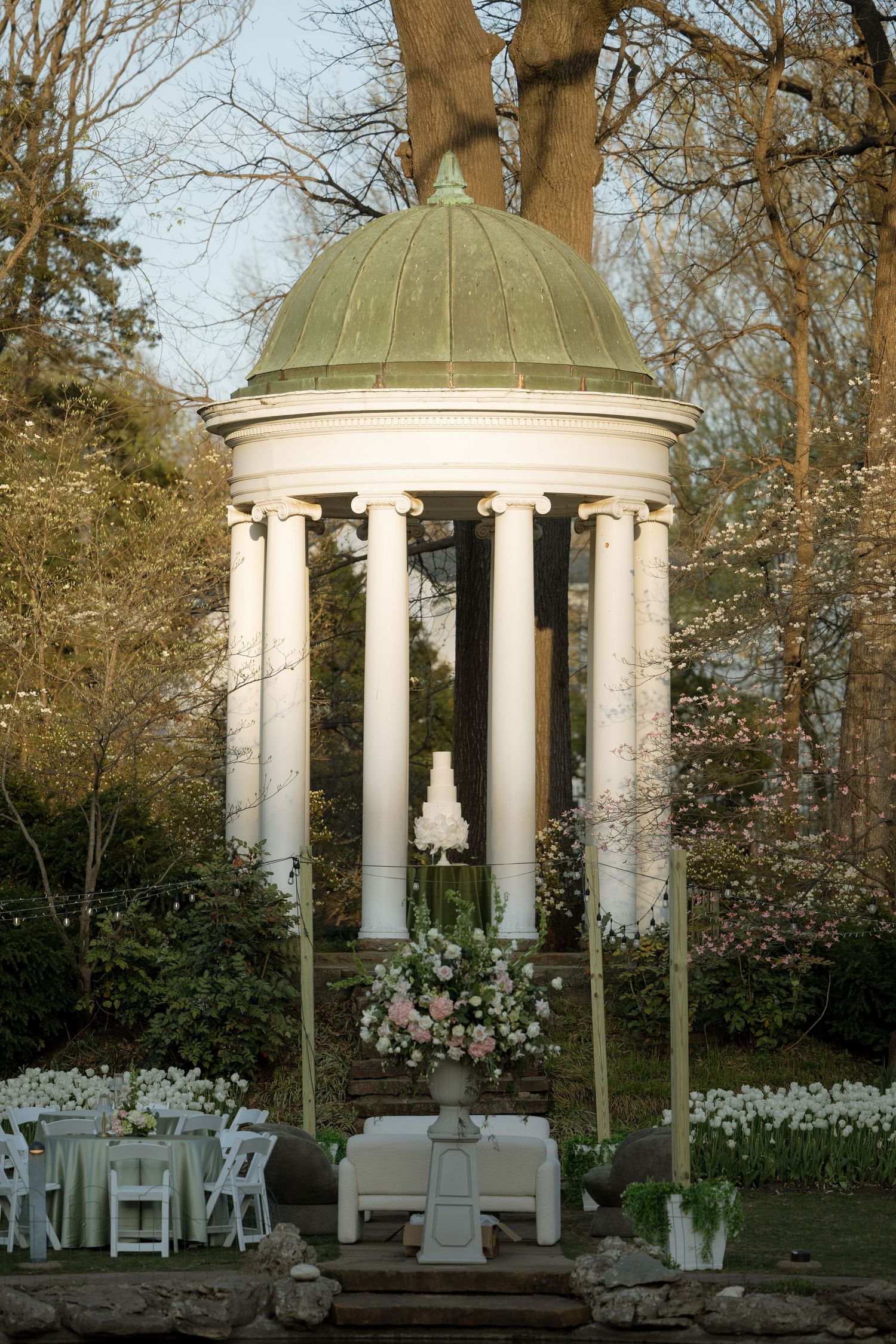 Elegant white rotunda wedding ceremony setup with floral arrangements and white chairs outdoors.