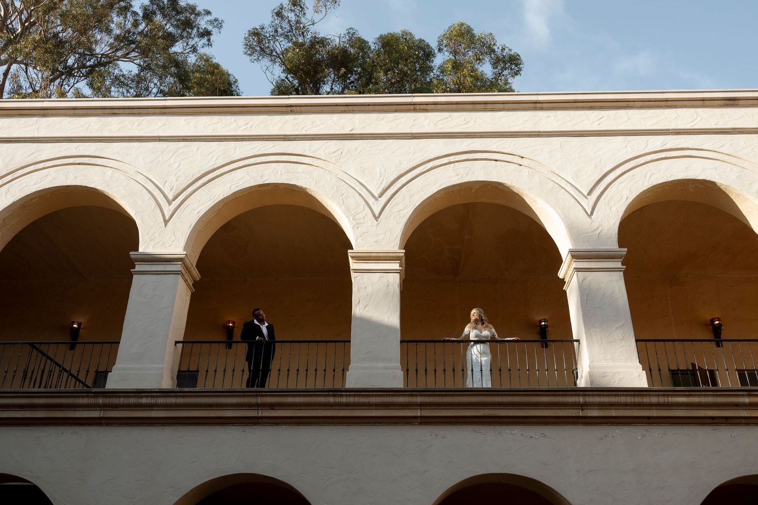 Classical stone colonnade with arched walkway and columns against blue sky.