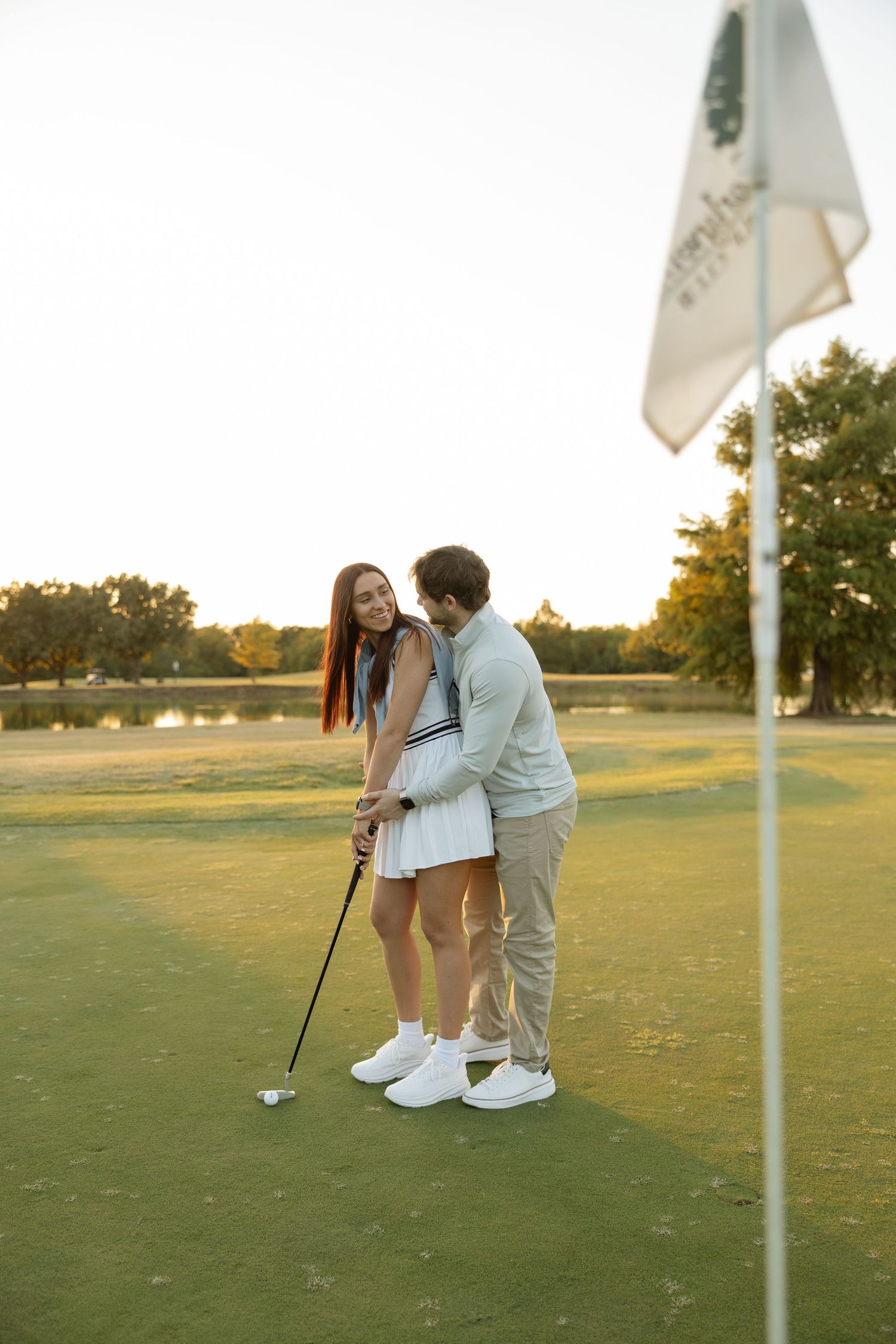 A playful golf lesson moment on a putting green with flag visible in golden hour light.