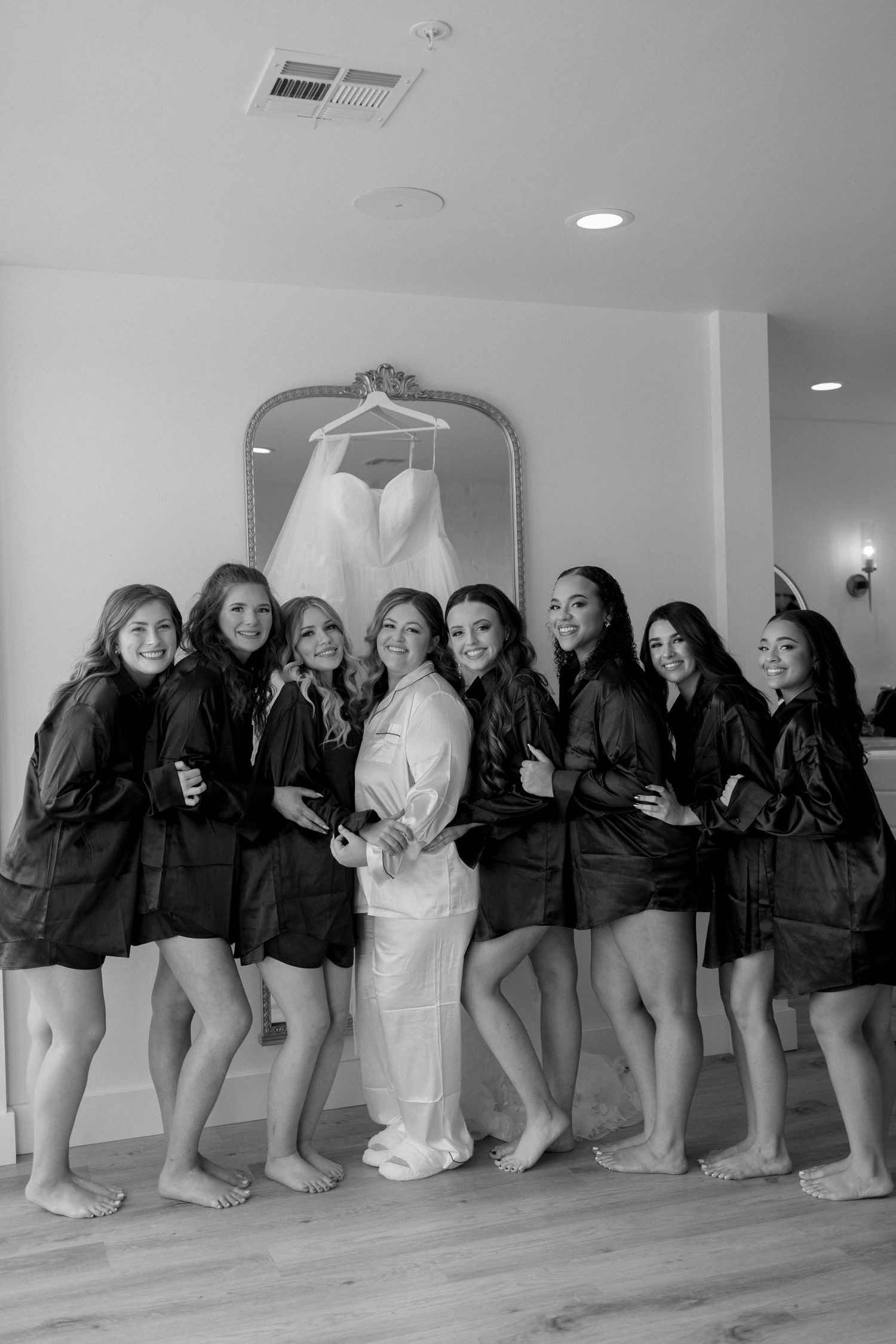 Group wearing matching black robes pose with wedding dress displayed in background.