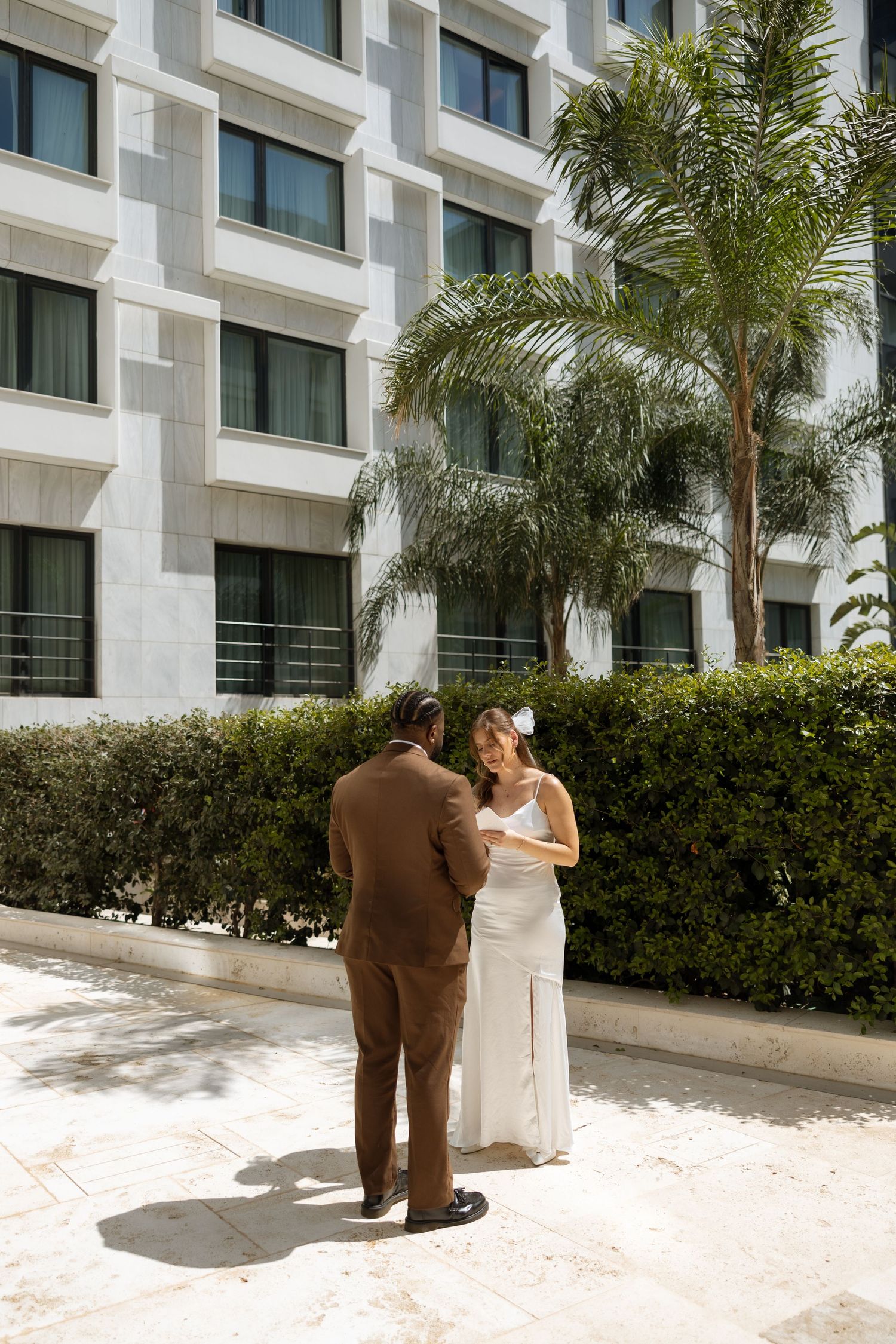 A couple shares a private moment against the backdrop of a modern hotel exterior.