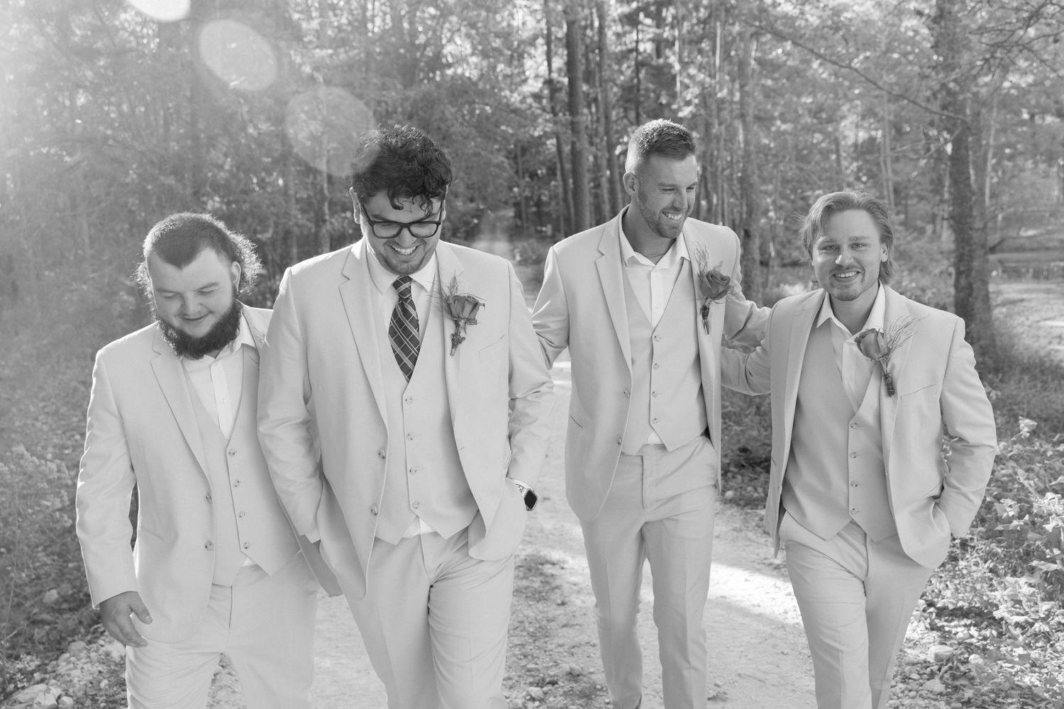 Black and white photo of four groomsmen in light suits walking together outdoors.